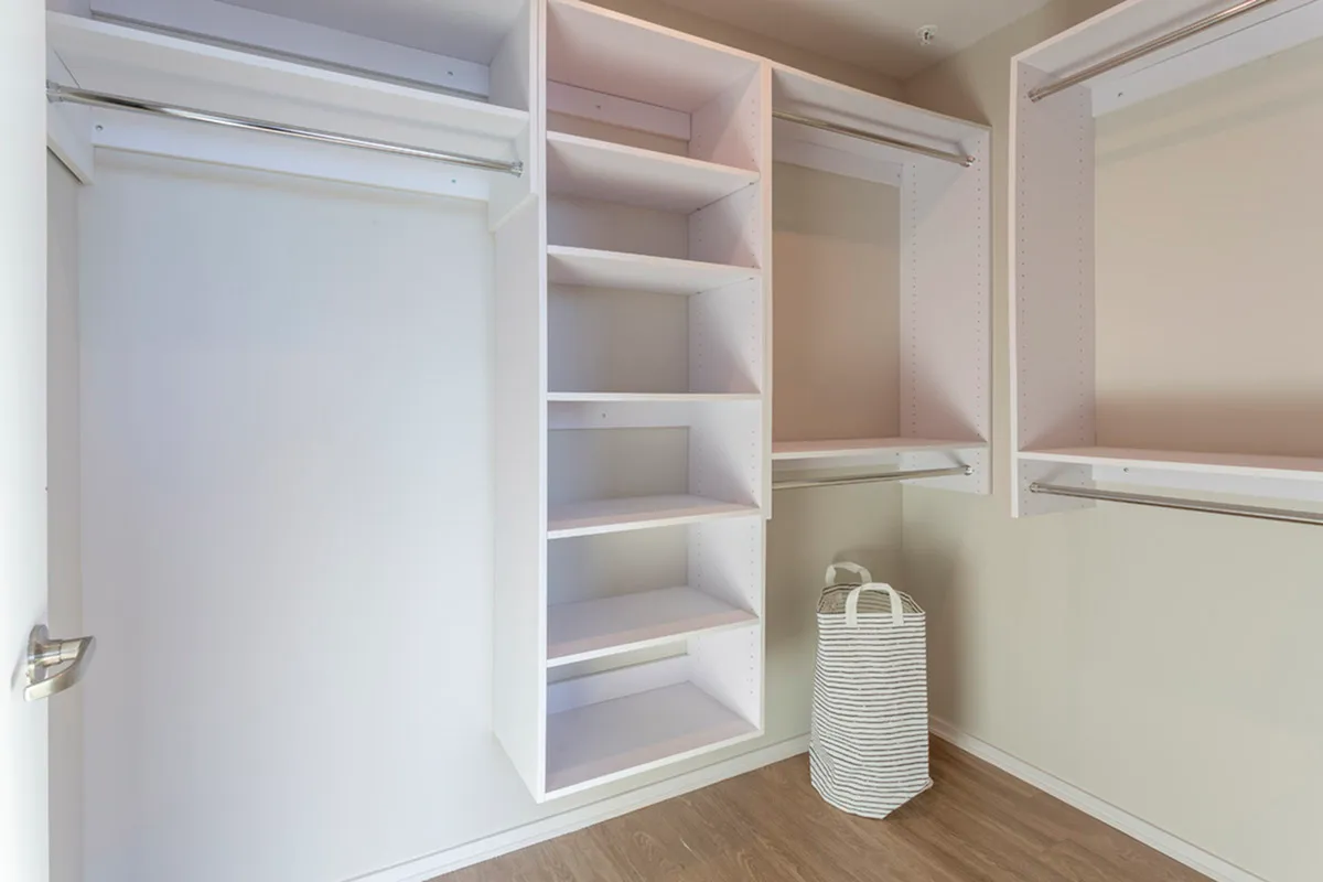 Sleek and modern walk-in closet with built-in white shelving, ample hanging space, and a stylish striped laundry basket on hardwood flooring.