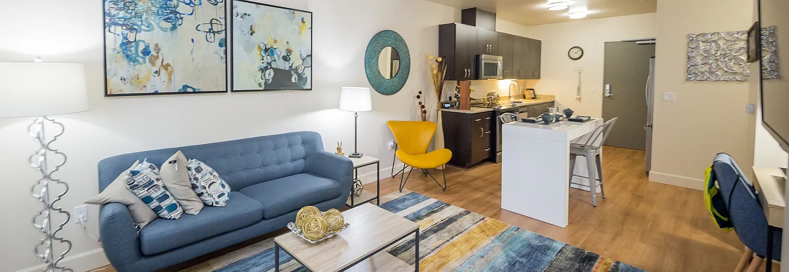 Modern living room with stylish decor, featuring a blue couch, colorful abstract art, and an open kitchen area.