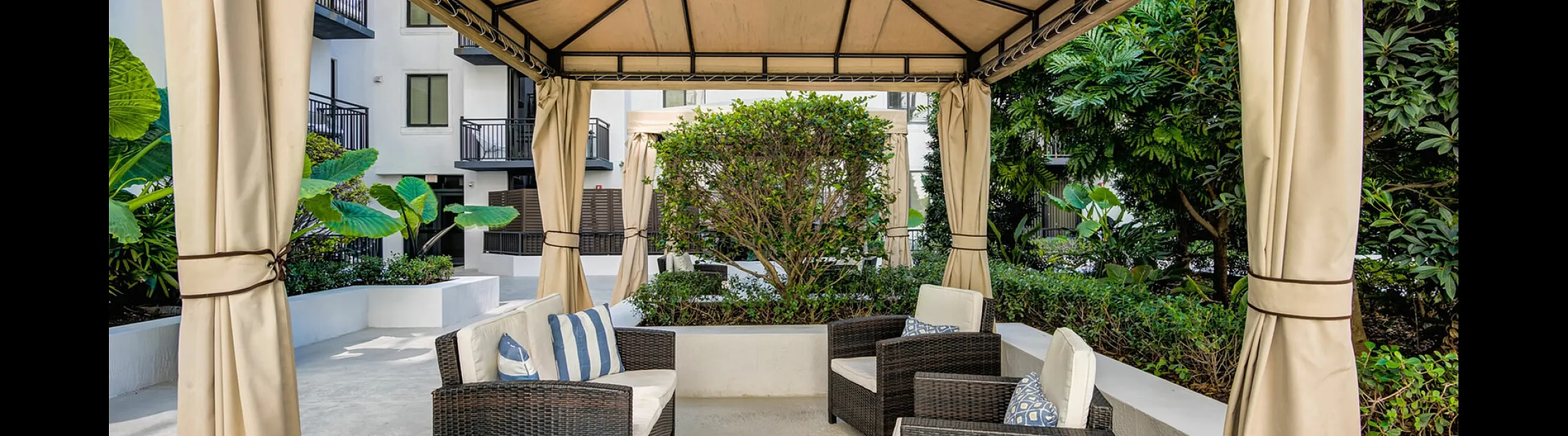 Elegant outdoor cabana with cozy wicker seating, lush greenery, and a tranquil ambiance for relaxation.