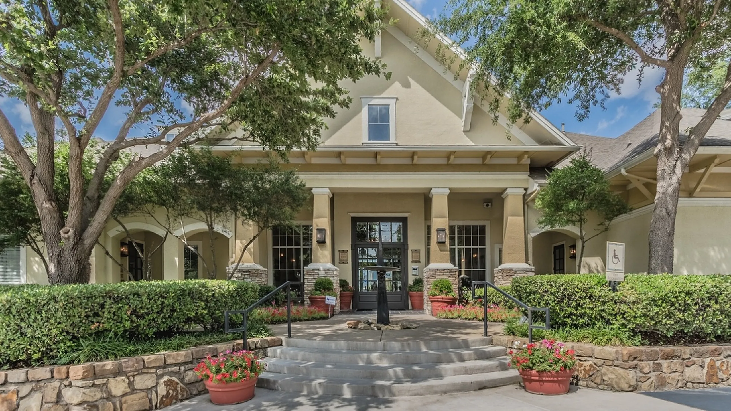 Charming apartment building entrance with lush greenery, classic stone accents, and inviting pathway, exuding elegance and comfort.