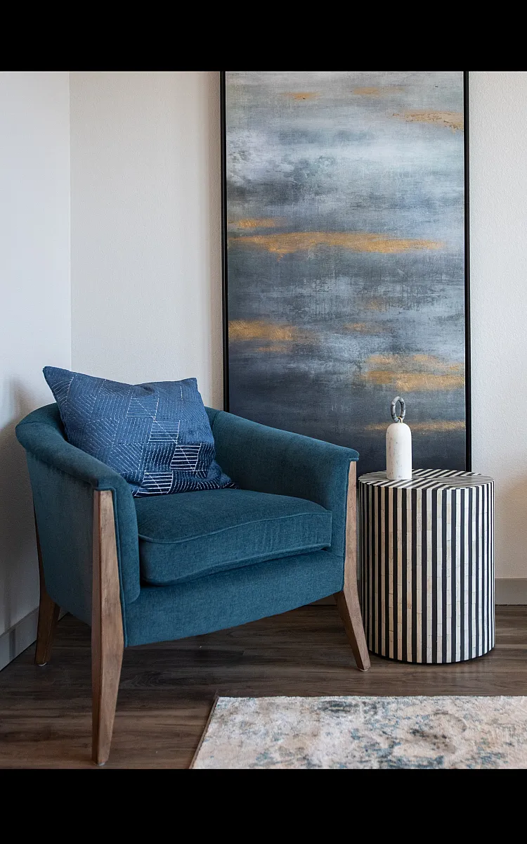 Chic living area with a modern blue armchair, striped side table, and elegant decor against a stylish abstract painting.