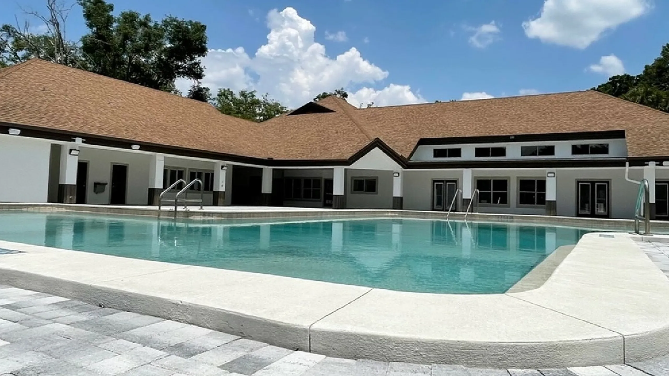 Inviting outdoor pool area with modern clubhouse under a bright blue sky, perfect for relaxation and leisure.