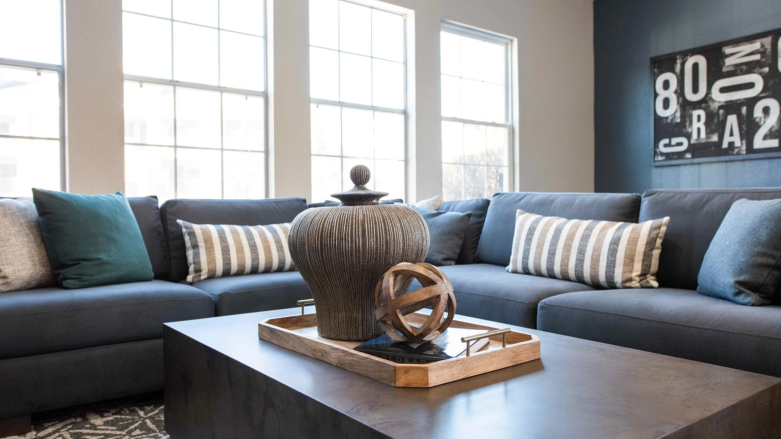 Contemporary living room featuring a stylish dark gray sectional sofa, elegant decorative accents, and abundant natural light from large windows.
