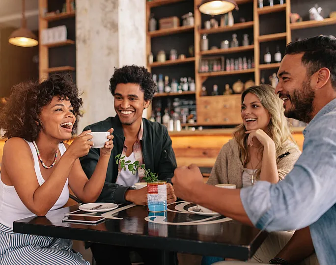 Group of friends enjoying a lively conversation at a cozy cafe, surrounded by warm decor and a friendly atmosphere.
