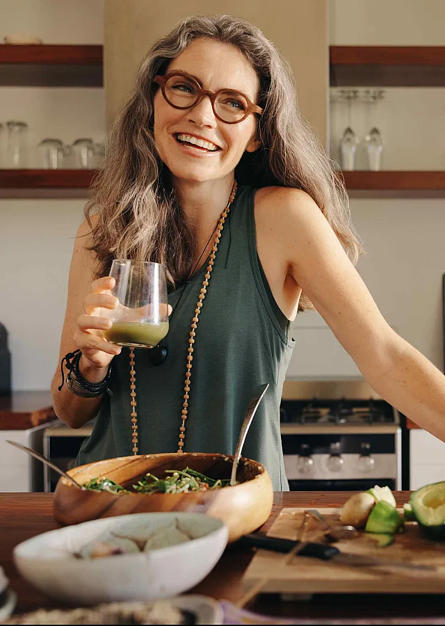 Bright and inviting kitchen with modern decor, featuring a person enjoying a fresh beverage, surrounded by healthy ingredients like avocados and limes on a wooden countertop.