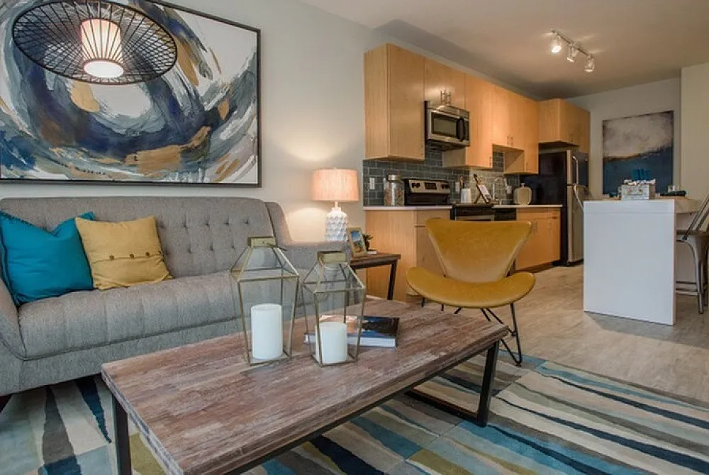 Chic and modern apartment living room with stylish decor, featuring a cozy sofa, vibrant artwork, and a sleek kitchen in the background.
