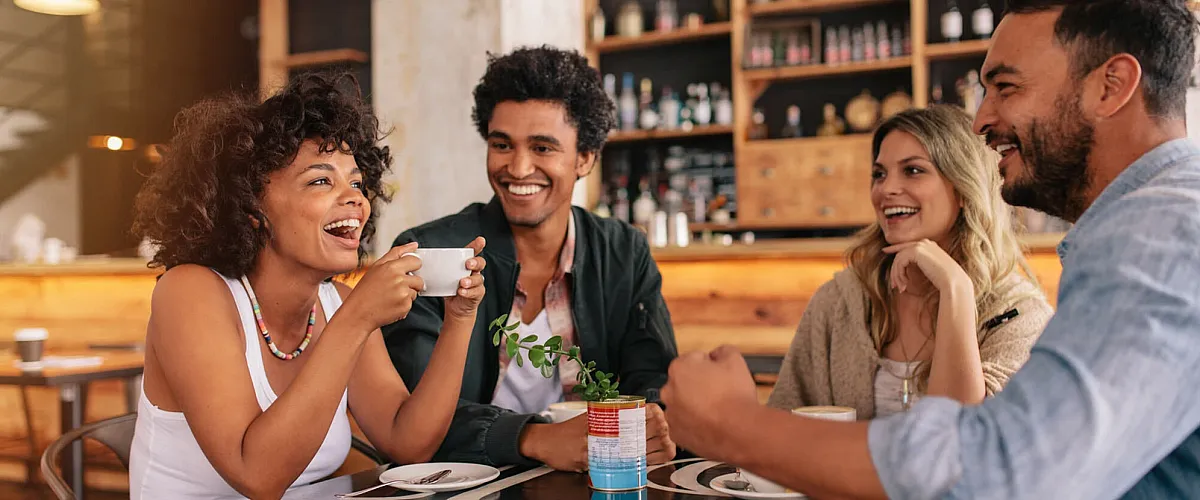 Joyful friends enjoying coffee together in a cozy cafe with modern decor and warm lighting.