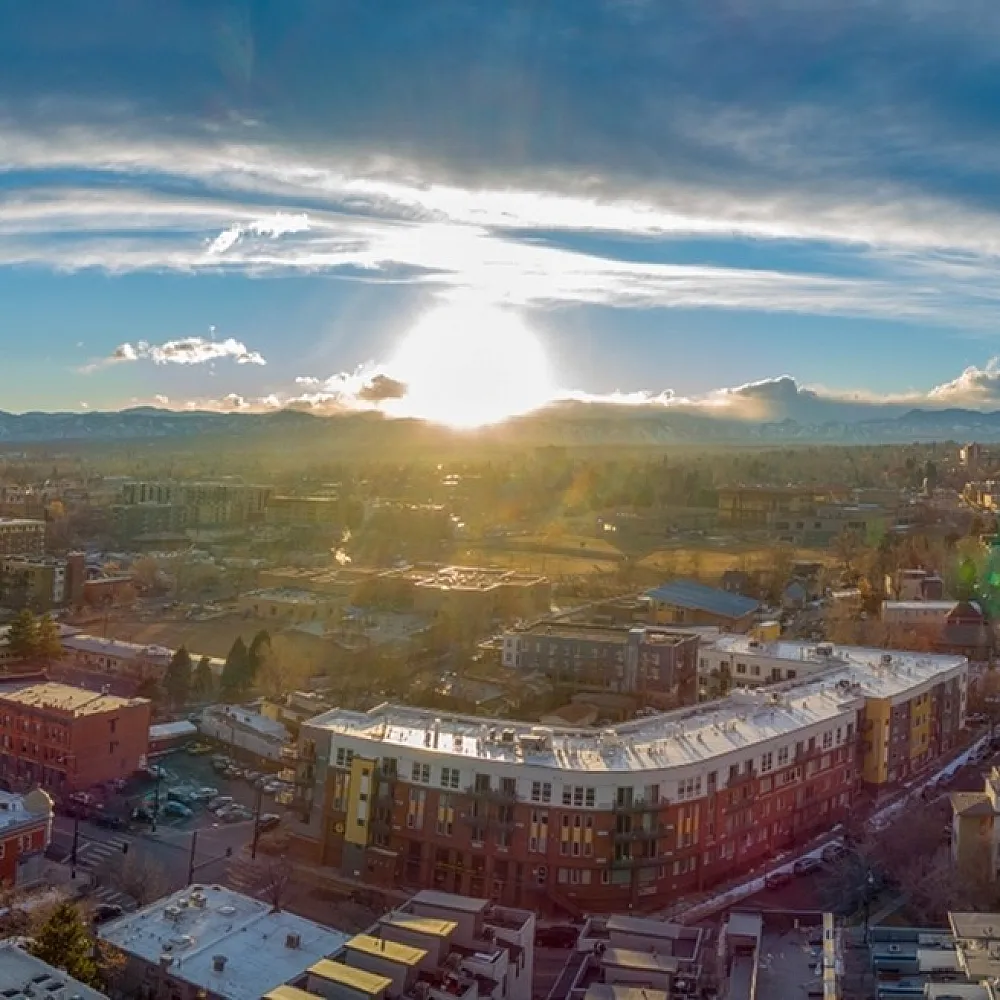 Breathtaking aerial view of a vibrant cityscape at sunset, highlighting modern apartments and snow-capped mountain vistas.