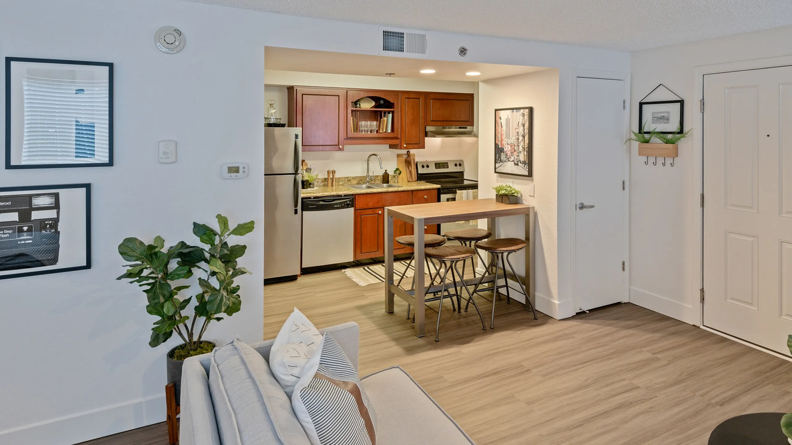 Chic apartment kitchen with sleek appliances, wooden cabinetry, and cozy breakfast bar, adjacent to a stylishly furnished living area for modern living.