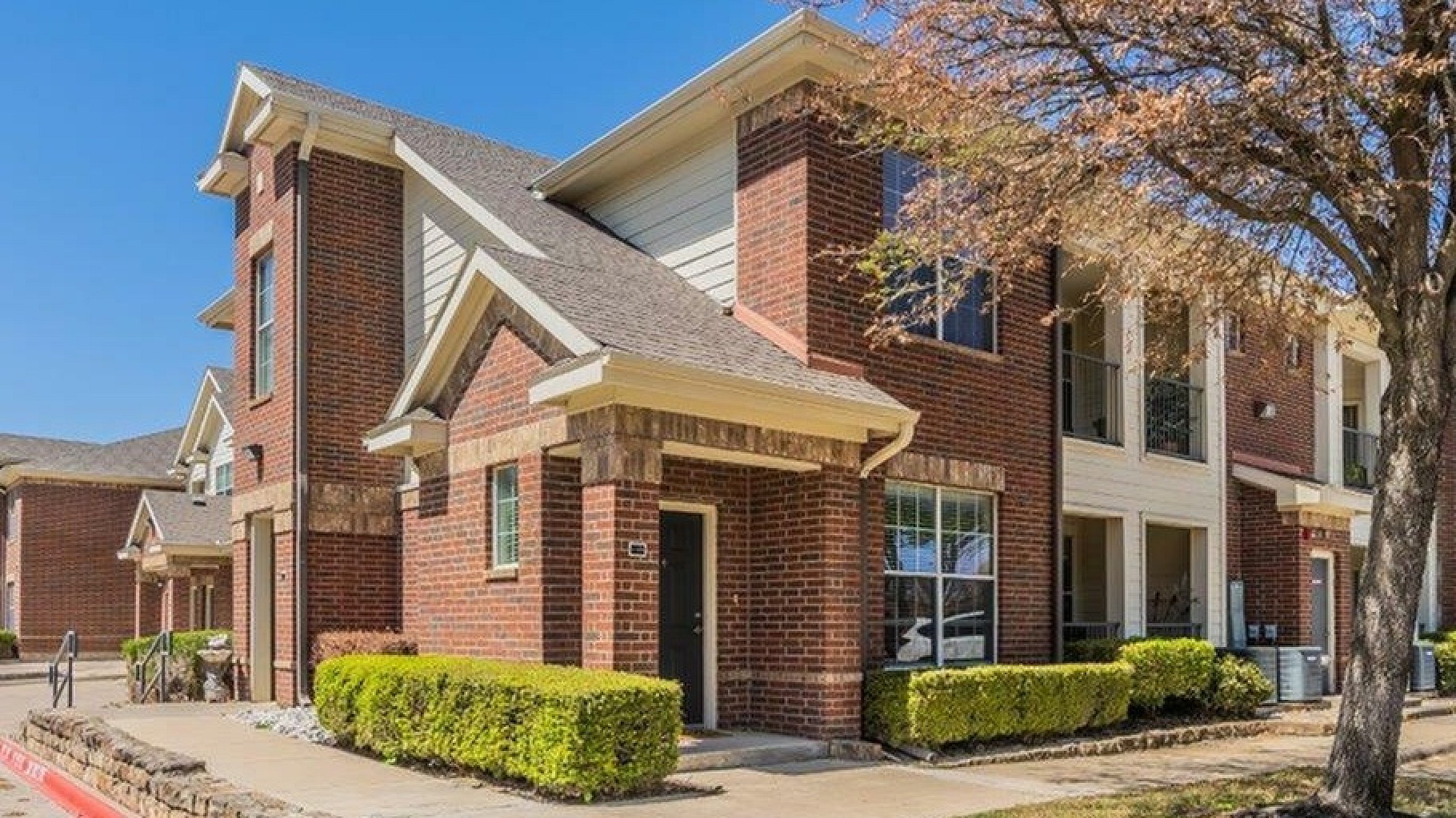 Charming red-brick apartment building with beautiful landscaping, showcasing a modern and inviting exterior on a sunny day.