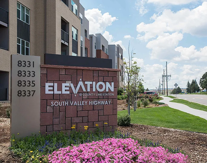 Elegant entry at Elevation @ County Line Station with vibrant flowers and modern architecture in a serene location on South Valley Highway.