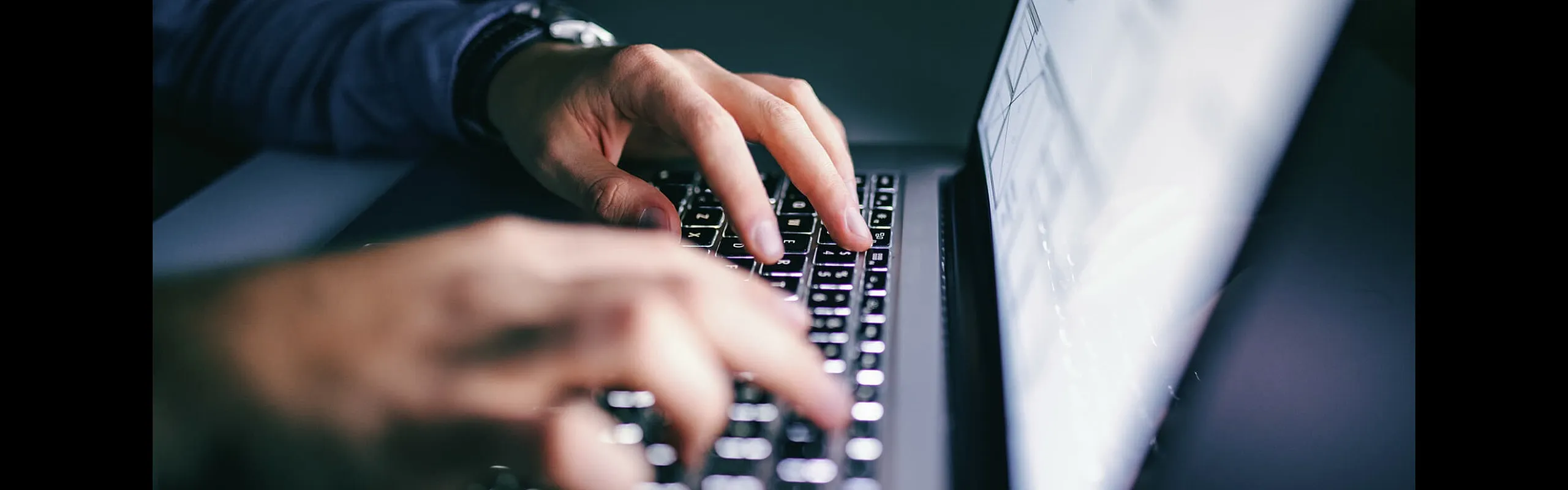 Close-up of hands typing on a sleek laptop keyboard with a glowing screen, showcasing modern technology and productivity.