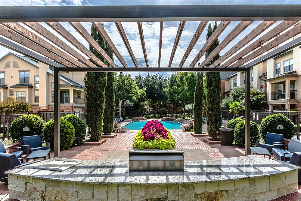 Charming outdoor space with a pergola, lush landscaping, and a sparkling swimming pool surrounded by stylish seating in a modern residential community.