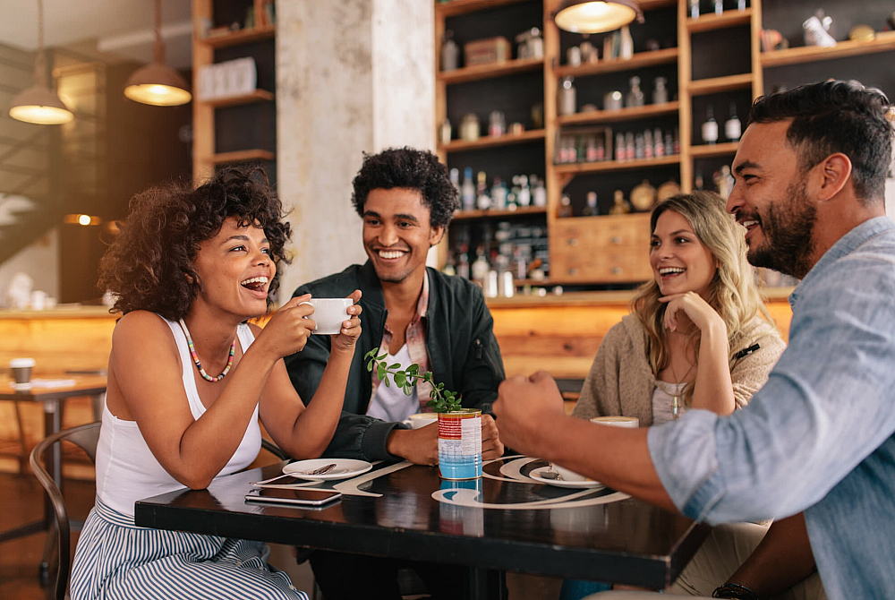 Vibrant cafe scene with four friends laughing and enjoying coffee, creating a warm and inviting atmosphere.