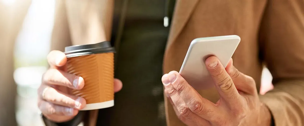 Chic urban lifestyle with a sleek smartphone and eco-friendly coffee cup in hand, perfect for modern city living.