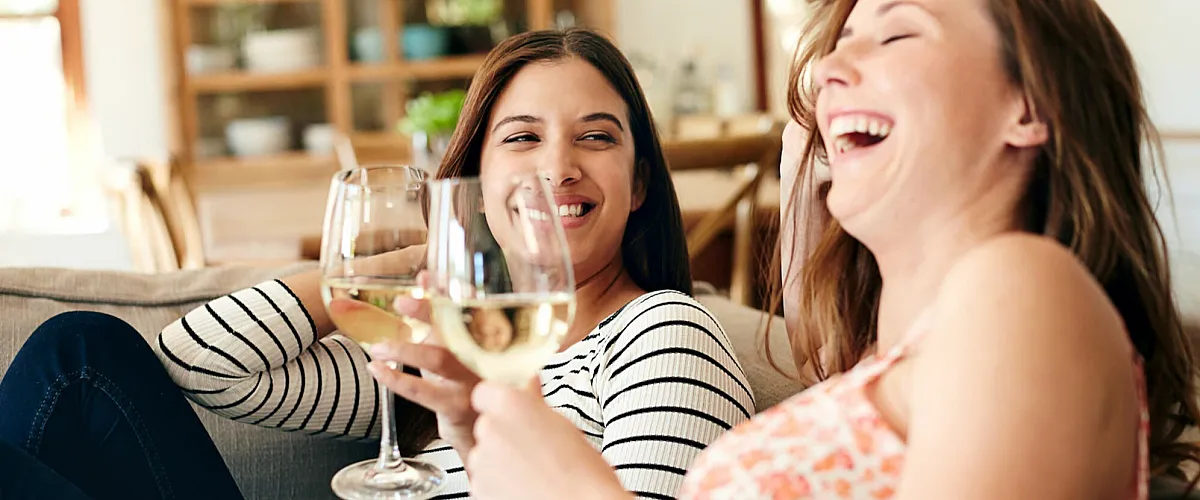 Joyful friends enjoying wine in a cozy, sunlit living room with elegant decor and a welcoming atmosphere.