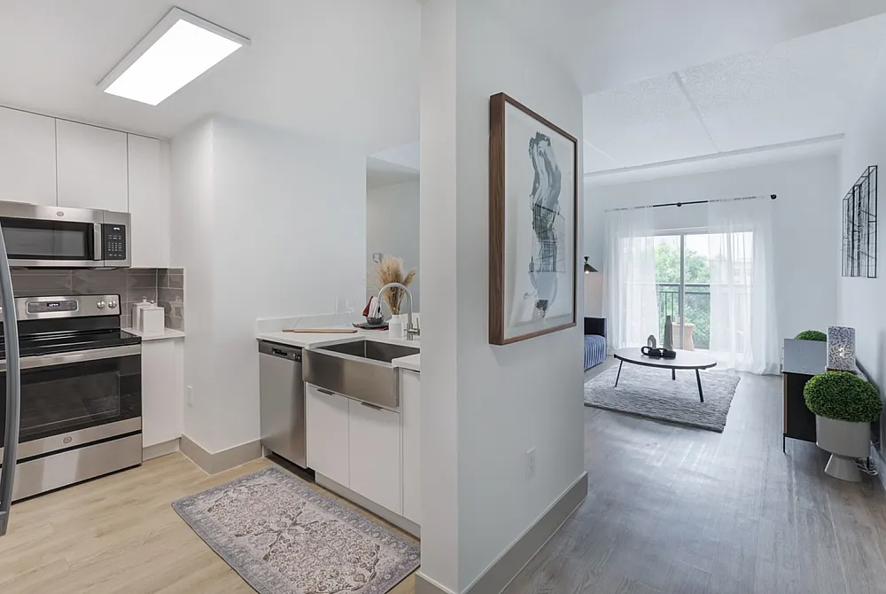 Modern kitchen with sleek stainless steel appliances leading to a bright living area with natural light and stylish decor.