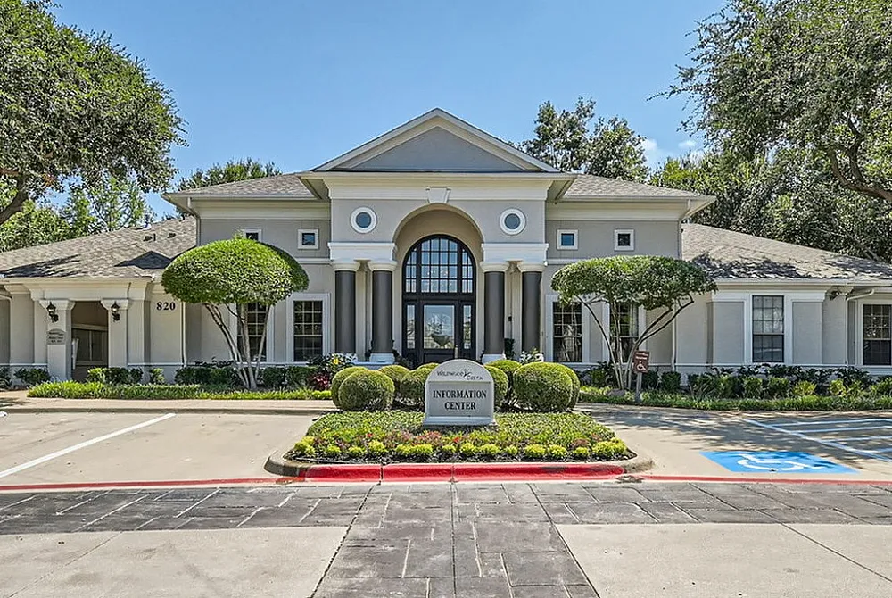 Elegant apartment complex entrance with manicured landscaping, a spacious driveway, and classic architectural design.