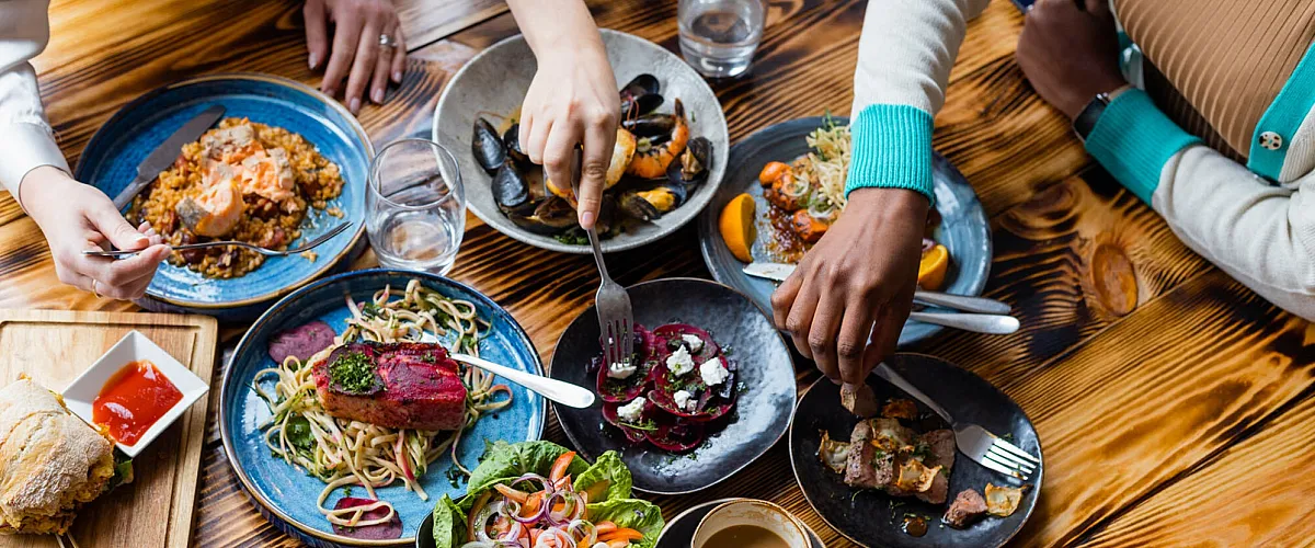 Vibrant overhead view of a shared dining experience with diverse, colorful dishes on a rustic wooden table.