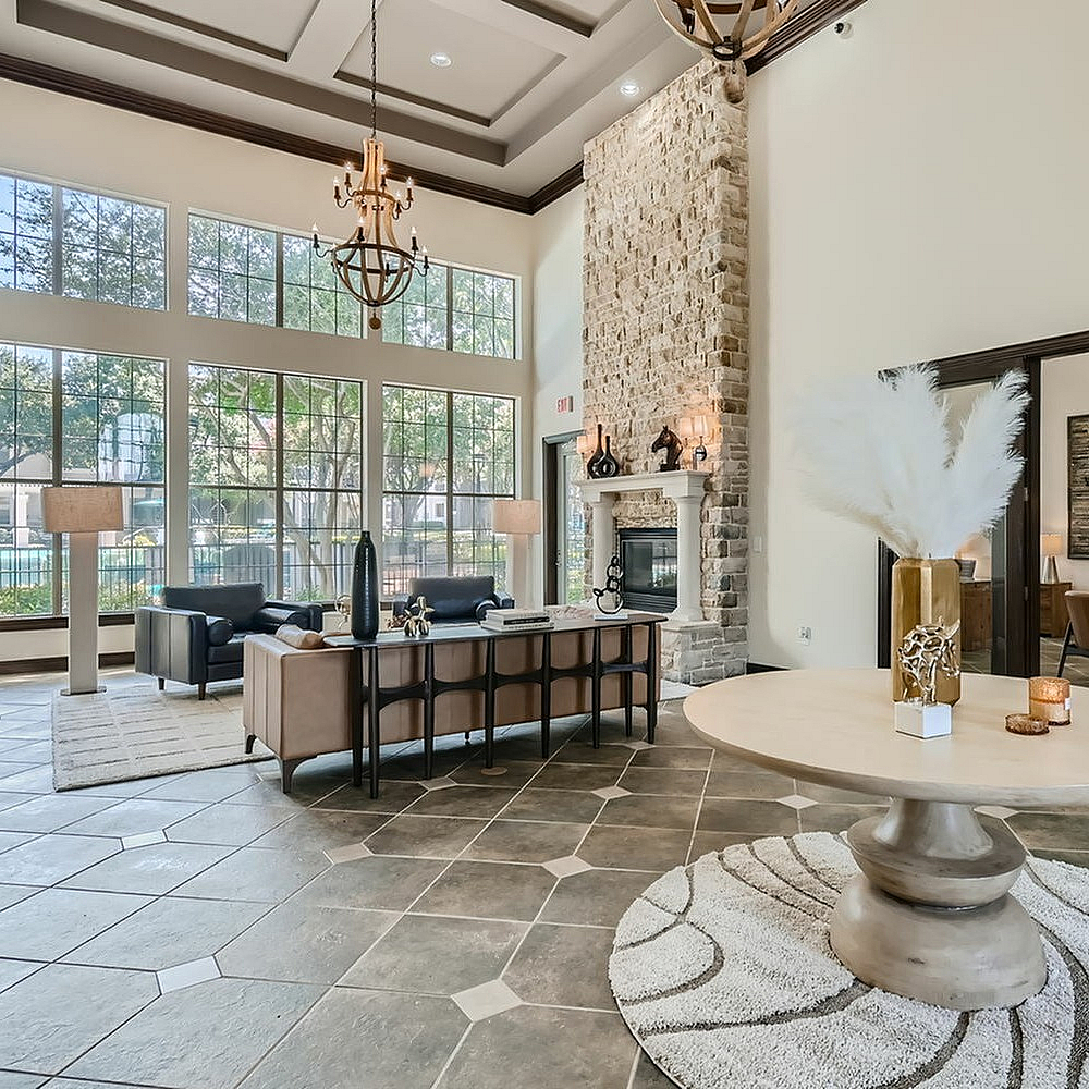Luxurious apartment lobby featuring high ceilings, large windows, elegant chandeliers, a stone fireplace, and modern decor.