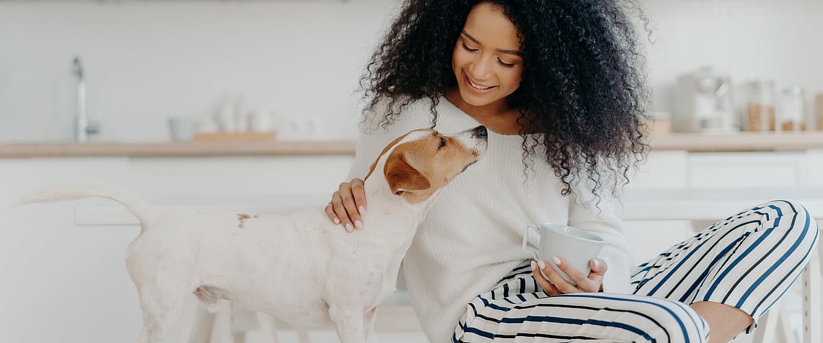 Cozy modern kitchen with a joyful woman enjoying coffee and bonding with her playful dog.
