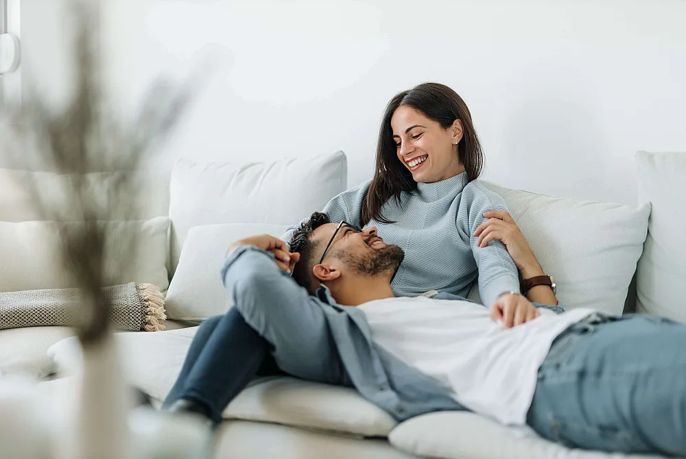 Happy couple relaxing together on a cozy, modern white sofa, basking in natural light.
