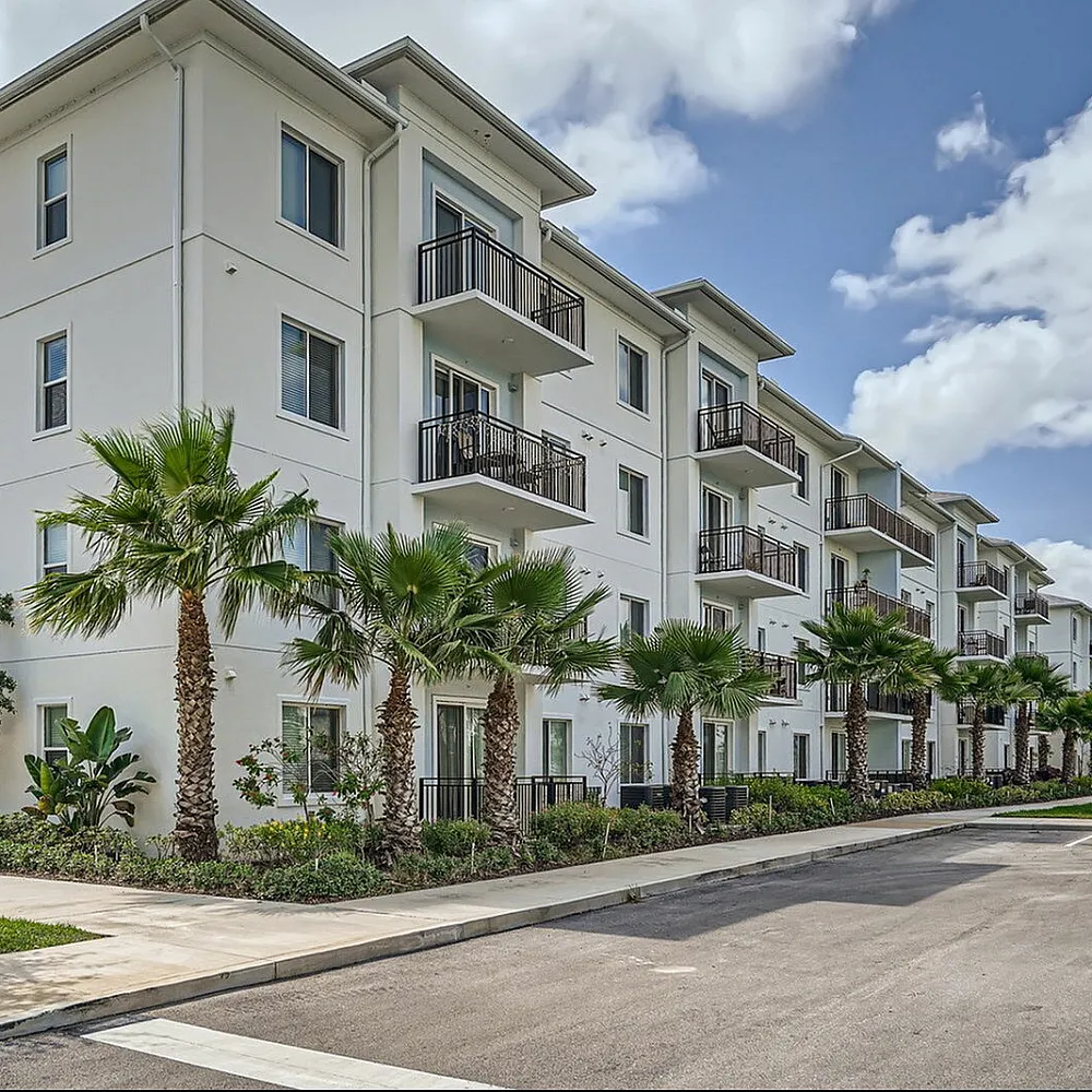 Modern apartment building with sleek balconies and lush palm trees, promising a stylish and vibrant living experience.