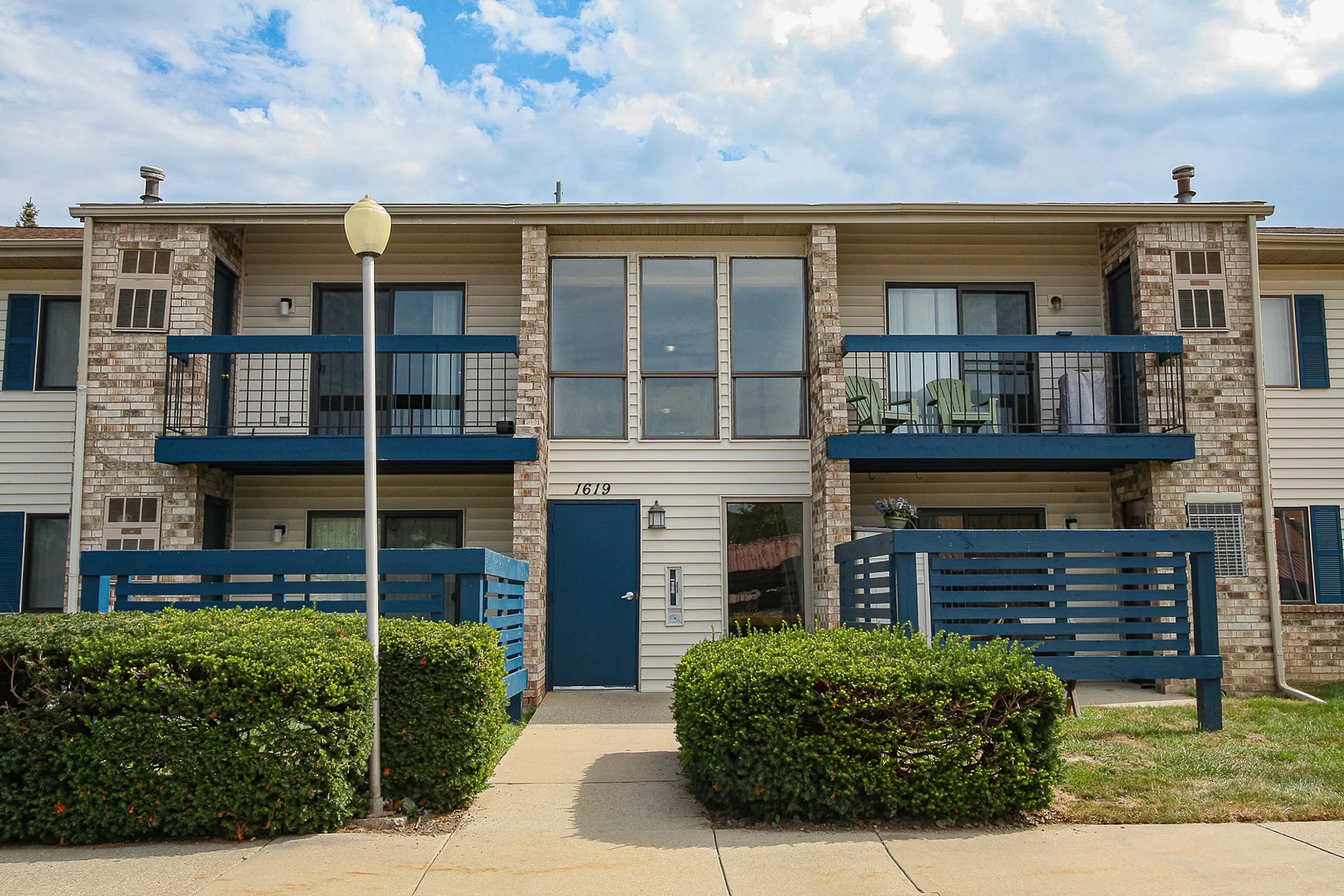 Charming two-story apartment building with modern blue accents, inviting balconies, and lush greenery.