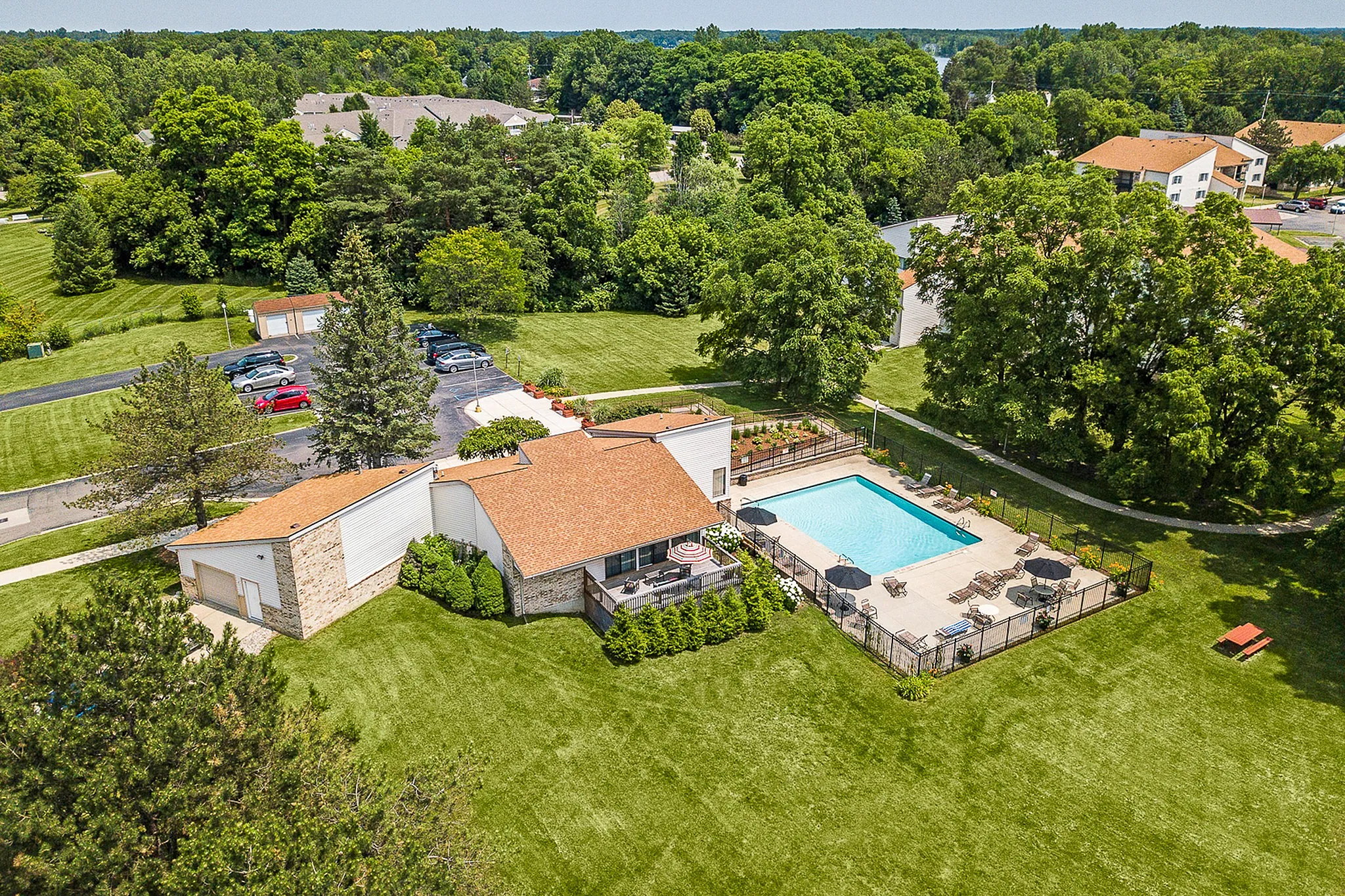 Beautiful aerial view of a residential complex featuring a vibrant community pool, lush green lawns, and ample parking surrounded by serene trees.