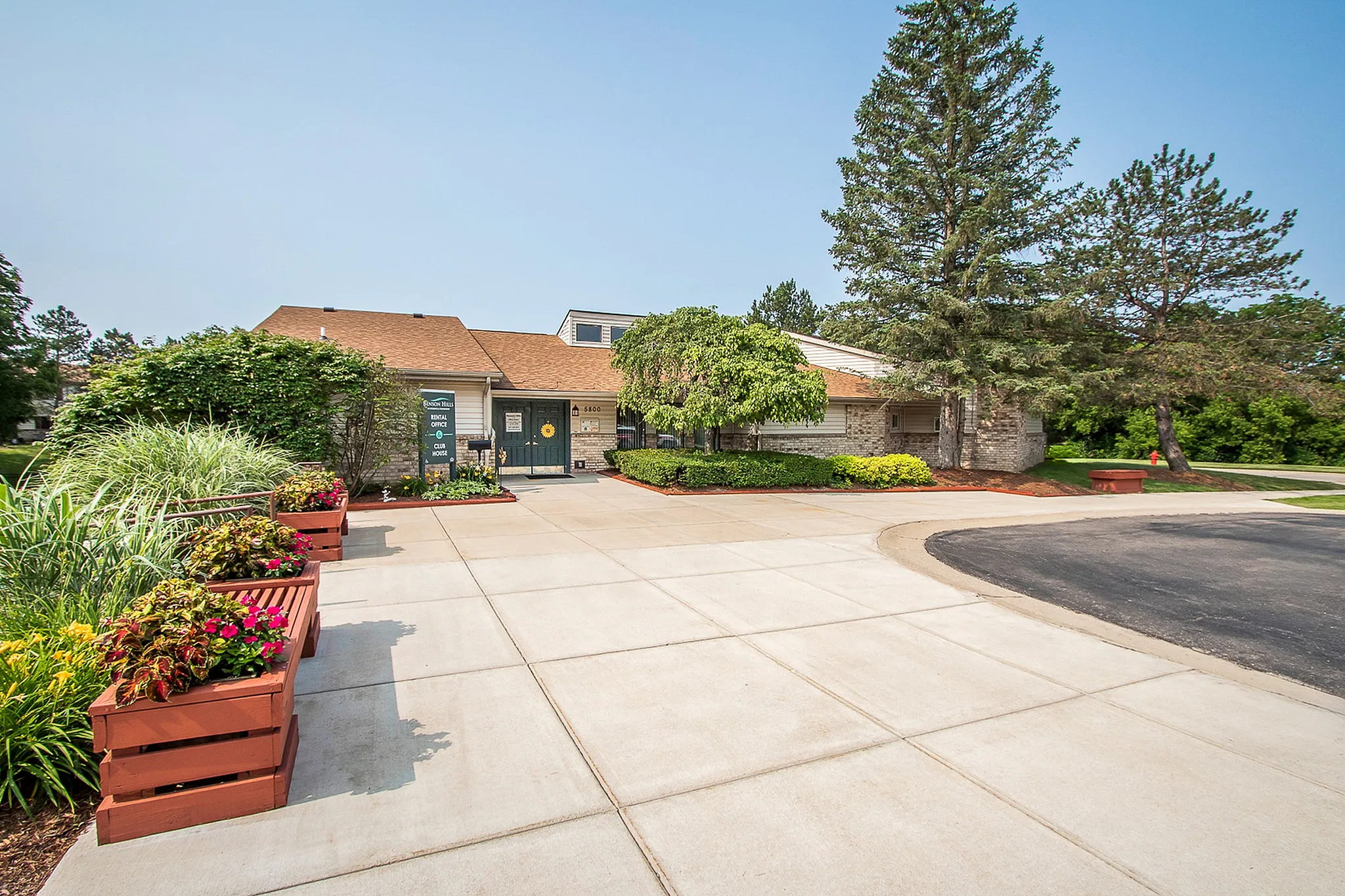 Charming community entrance with lush greenery, vibrant flower planters, and a welcoming clubhouse facade.