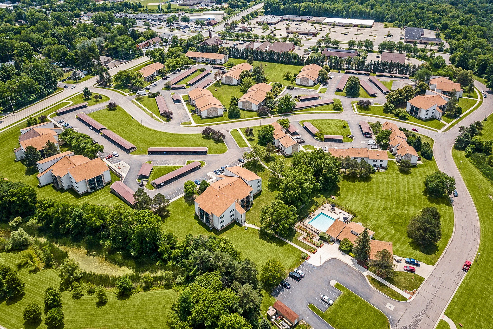 Scenic aerial view of a charming residential community featuring clustered buildings with orange roofs, lush green lawns, and a sparkling swimming pool.
