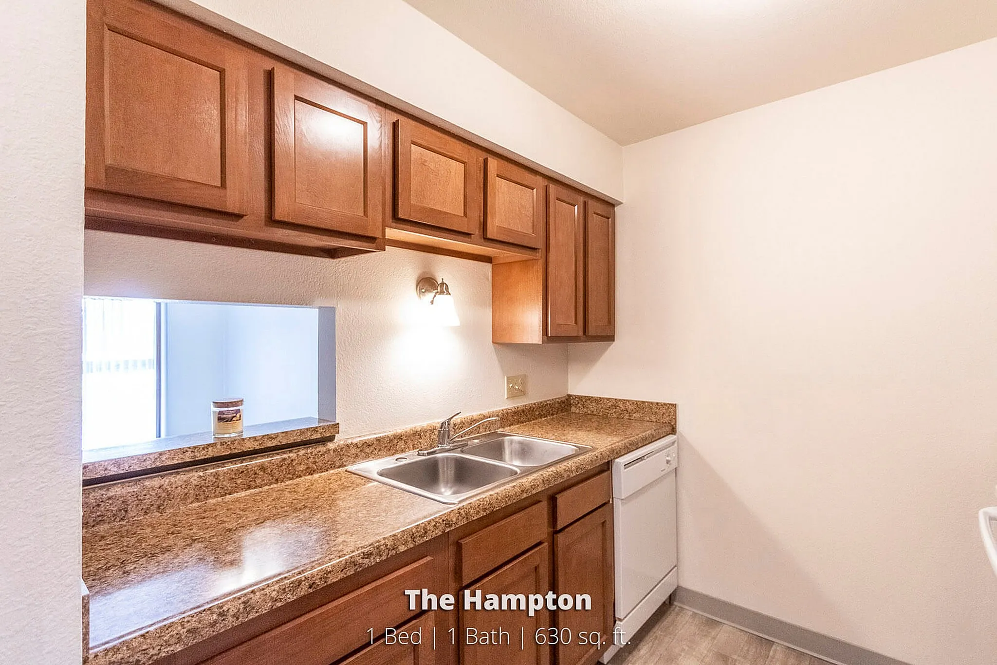 Charming kitchen in The Hampton apartment featuring warm wooden cabinetry, a sleek granite countertop, and modern appliances. 1 Bed, 1 Bath, 630 sq. ft.