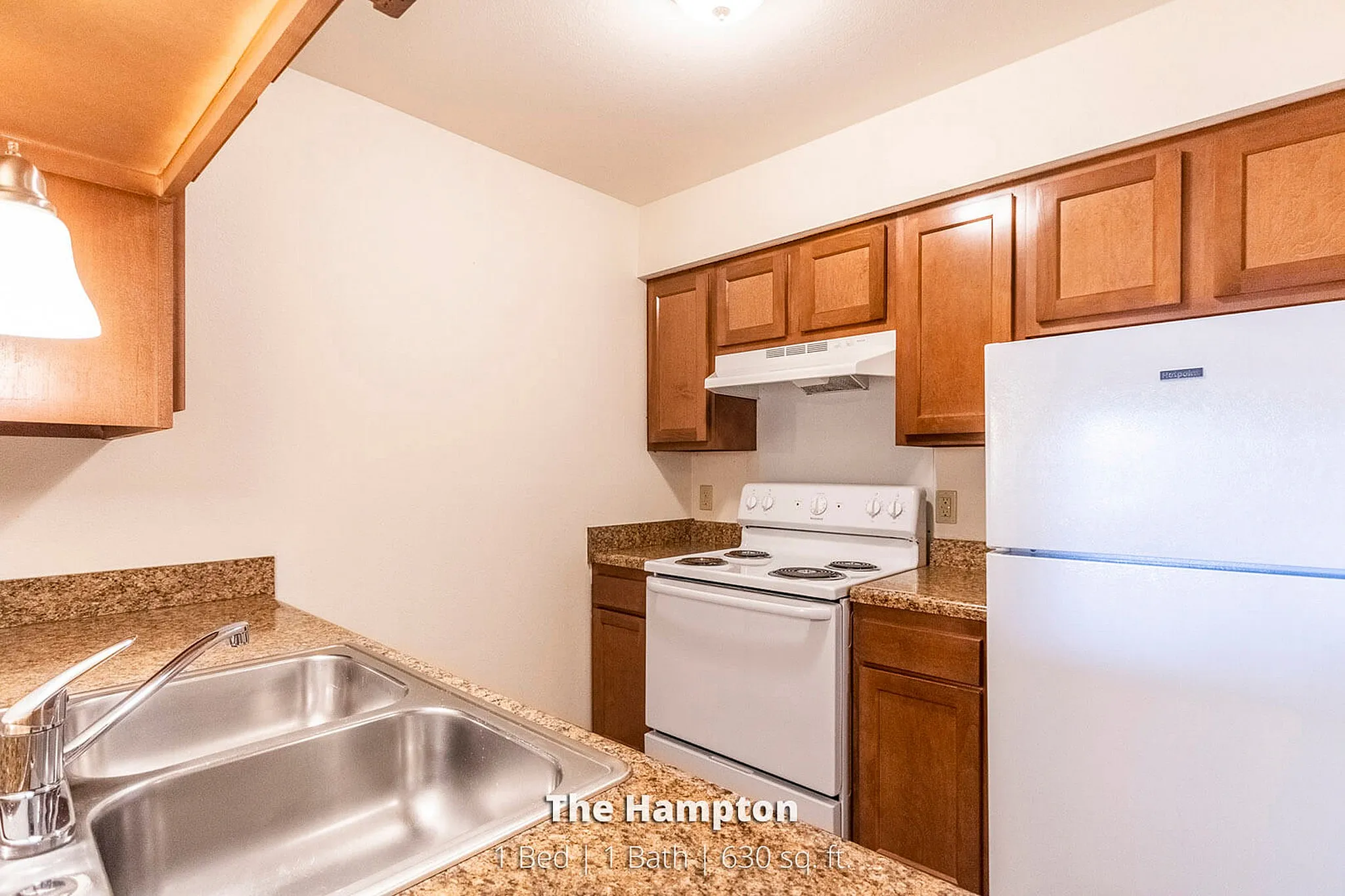 Warm and inviting kitchen in The Hampton, featuring sleek granite countertops, modern appliances, and ample wooden cabinetry. 1 bed, 1 bath, 630 sq. ft.