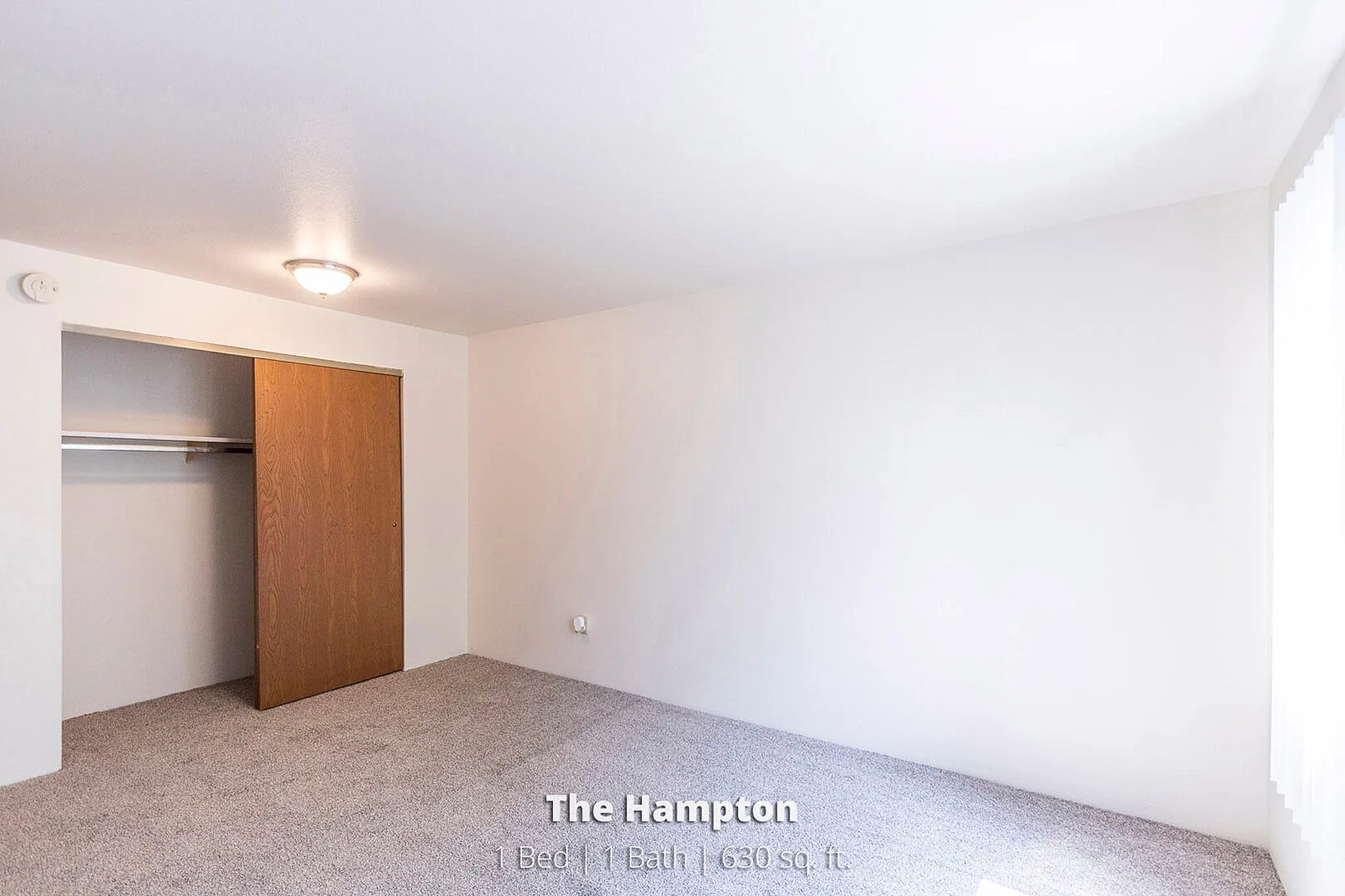 Bright and spacious bedroom in The Hampton, featuring plush carpeting and a generous closet, ideal for comfortable living.