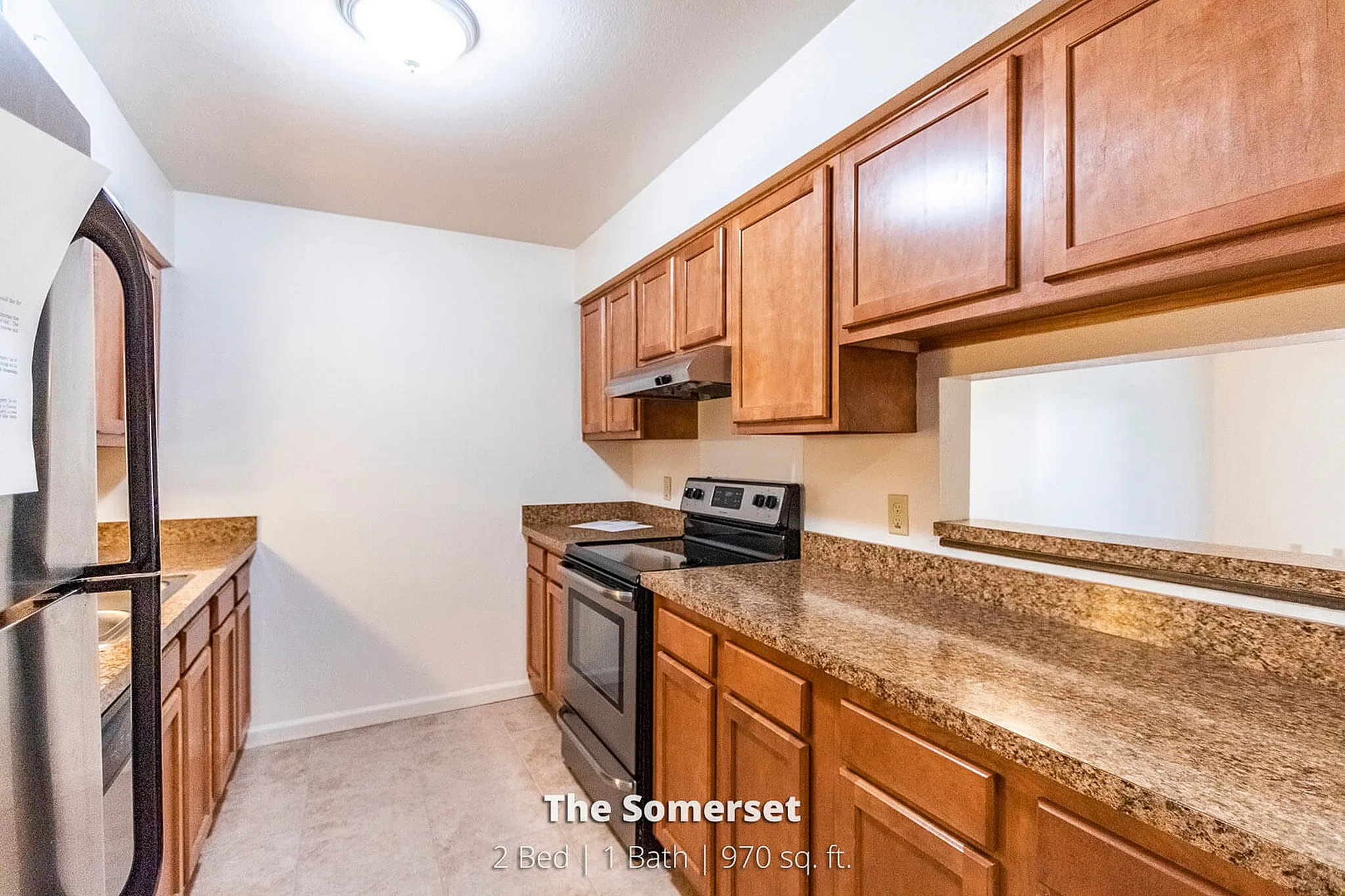 Charming kitchen in The Somerset apartment, featuring sleek granite countertops, rich wooden cabinetry, and modern appliances in a cozy 970 sq. ft. space.