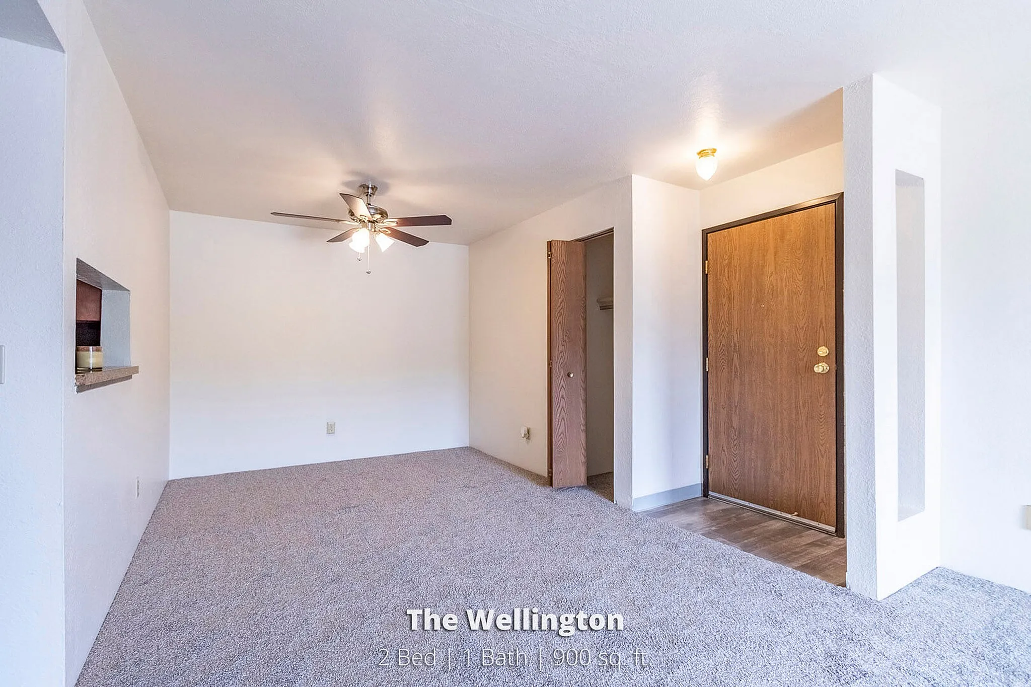 Inviting living space at The Wellington featuring plush carpet, ceiling fan, and warm wood accents, perfect for comfortable living.