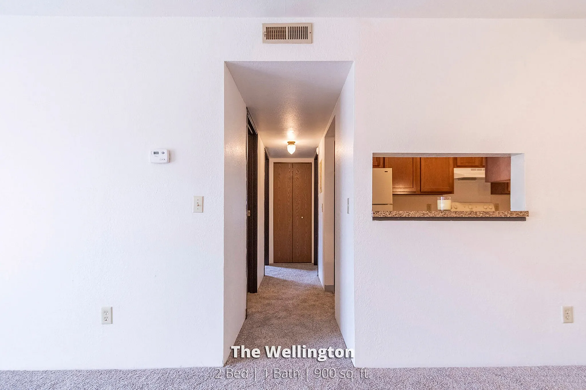 Inviting apartment entryway leading to a cozy kitchen with warm wooden cabinetry, part of The Wellington's 2 bed, 1 bath, 900 sq. ft. layout.