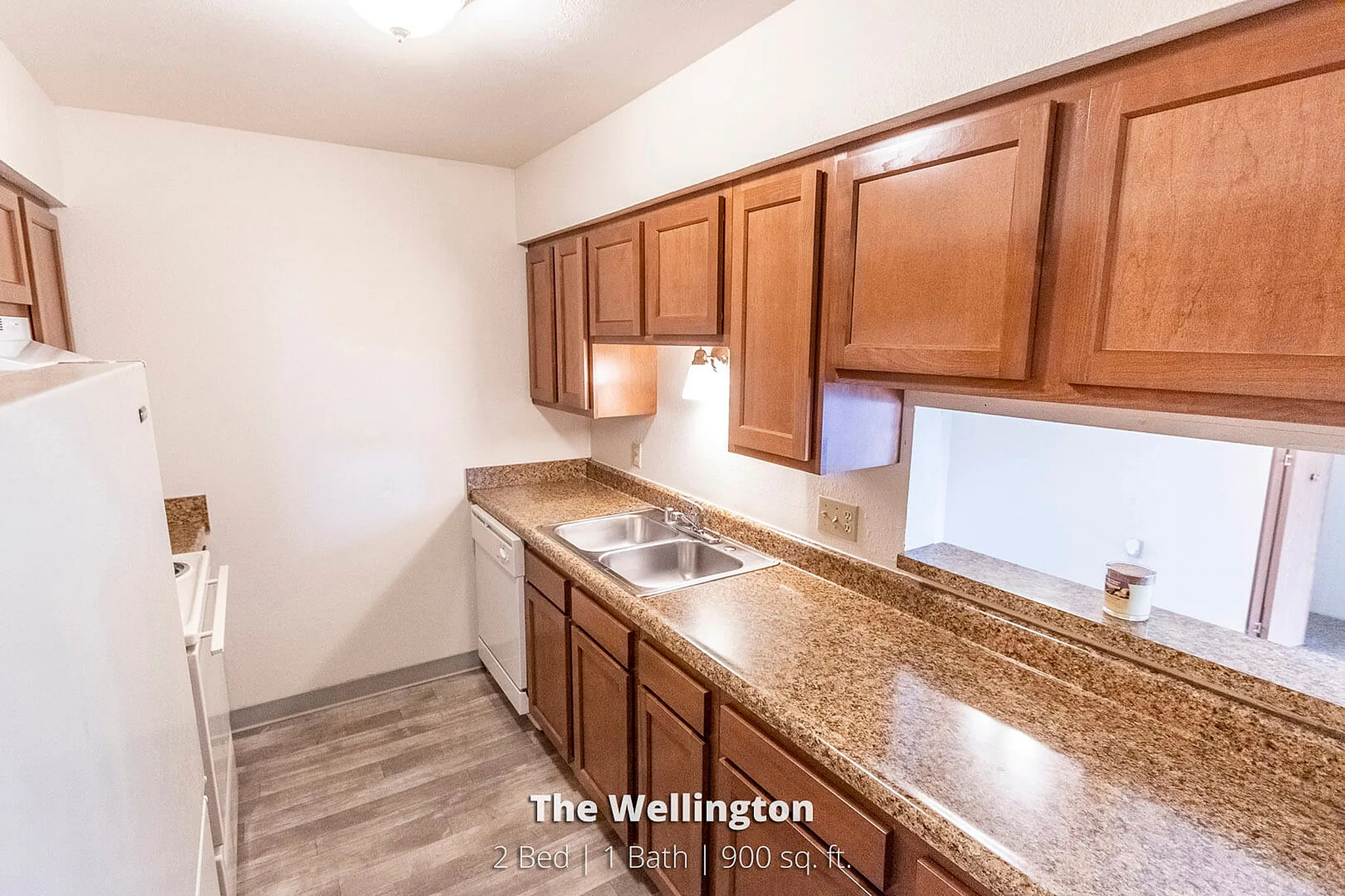 Modern kitchen at The Wellington with sleek granite countertops, ample cabinetry, and a large double sink, part of a 2 bed, 1 bath, 900 sq. ft. apartment.
