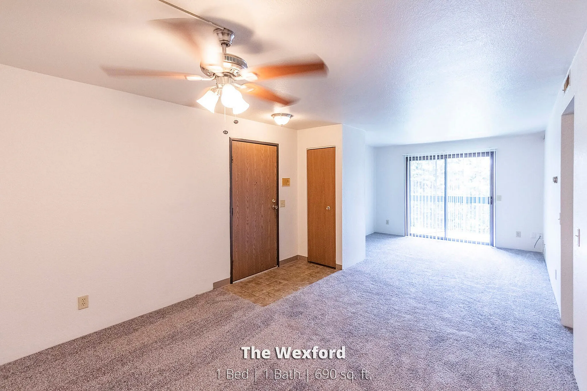 Bright and spacious living area in The Wexford apartment, featuring 1 bed and 1 bath, with large windows and cozy carpeted floors, 690 sq ft.