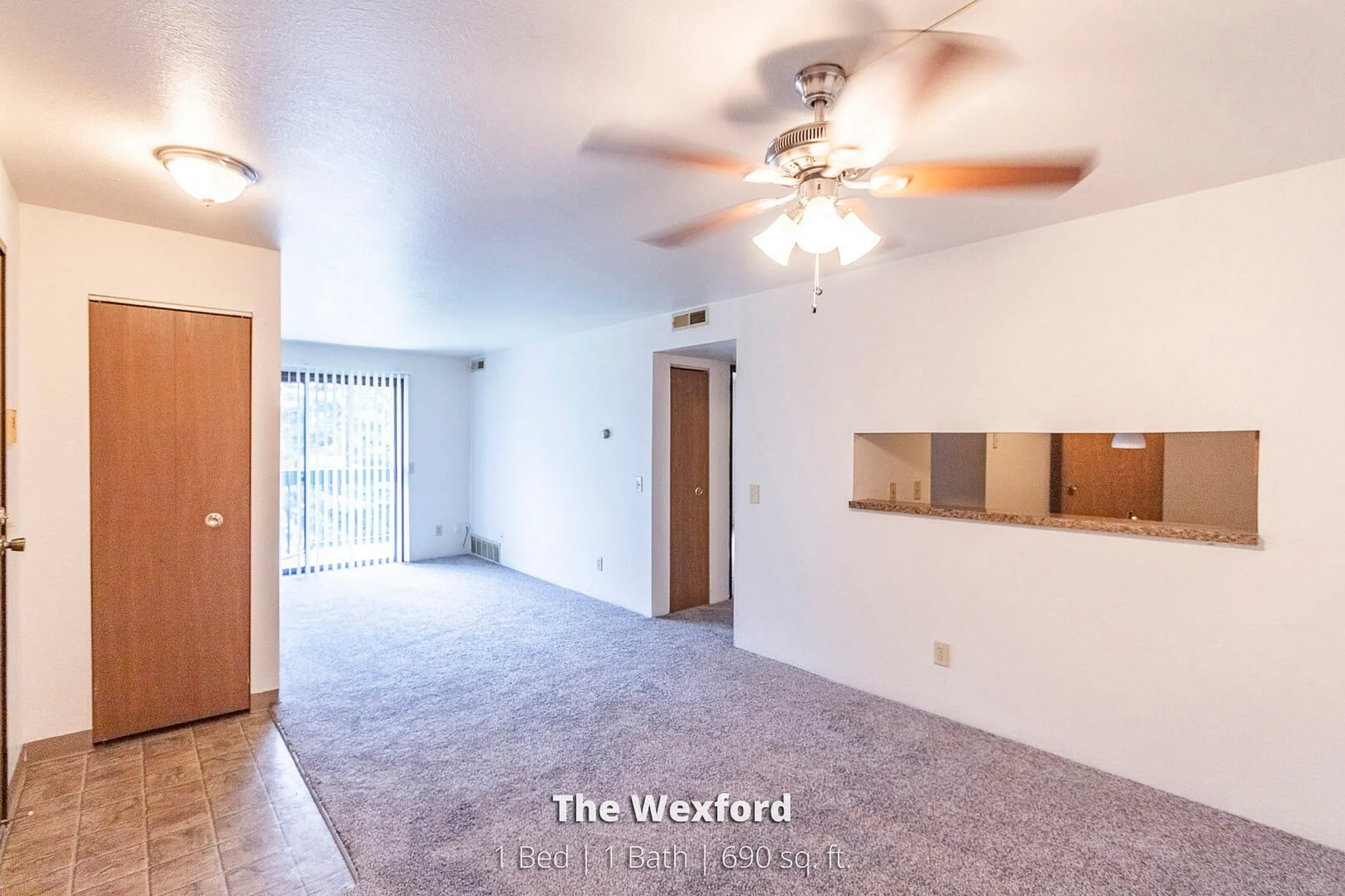 Bright and inviting living space in The Wexford with plush carpet, modern ceiling fan, and sliding balcony doors. Cozy 1-bedroom apartment, perfect for comfort and style in 690 sq. ft.