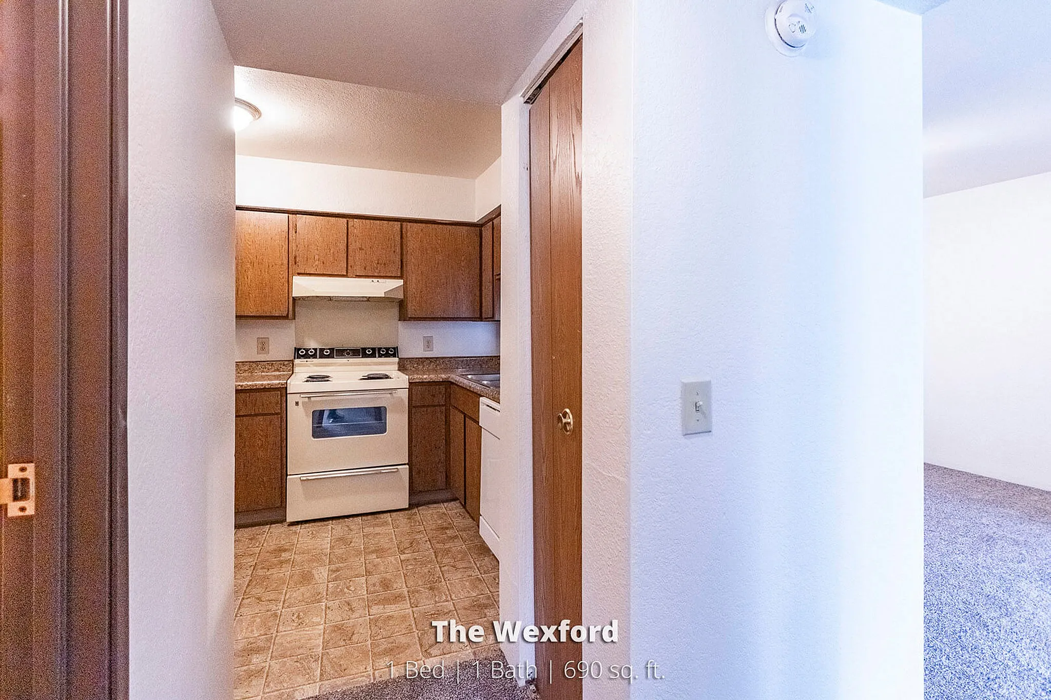 Cozy and efficient kitchen in 'The Wexford' apartment, featuring warm wooden cabinets and modern white appliances, perfect for comfortable living in a 1 Bed, 1 Bath, 690 sq. ft. space.