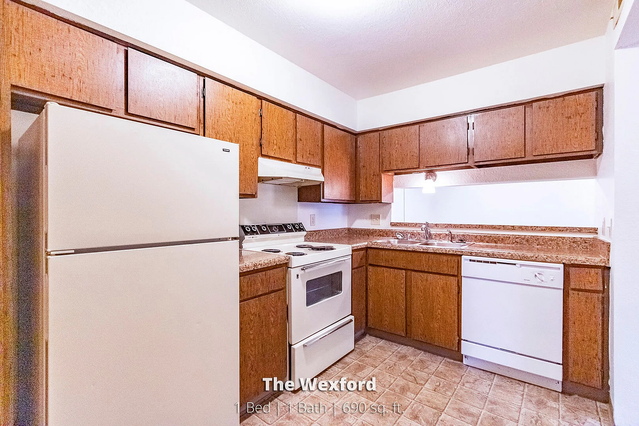Inviting kitchen in The Wexford, featuring spacious wooden cabinetry and modern appliances. 1 bedroom, 1 bath apartment with 690 sq. ft. offering functionality and style.