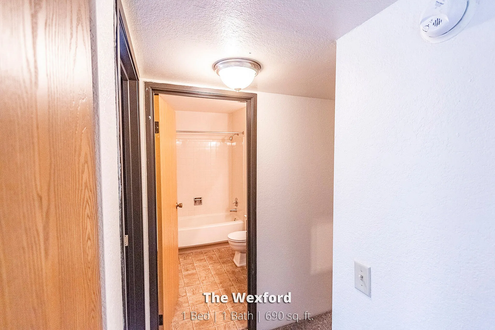 Inviting hallway leading to a well-lit bathroom with classic tiles, inside The Wexford's cozy 1 bed, 1 bath unit spanning 690 sq. ft.