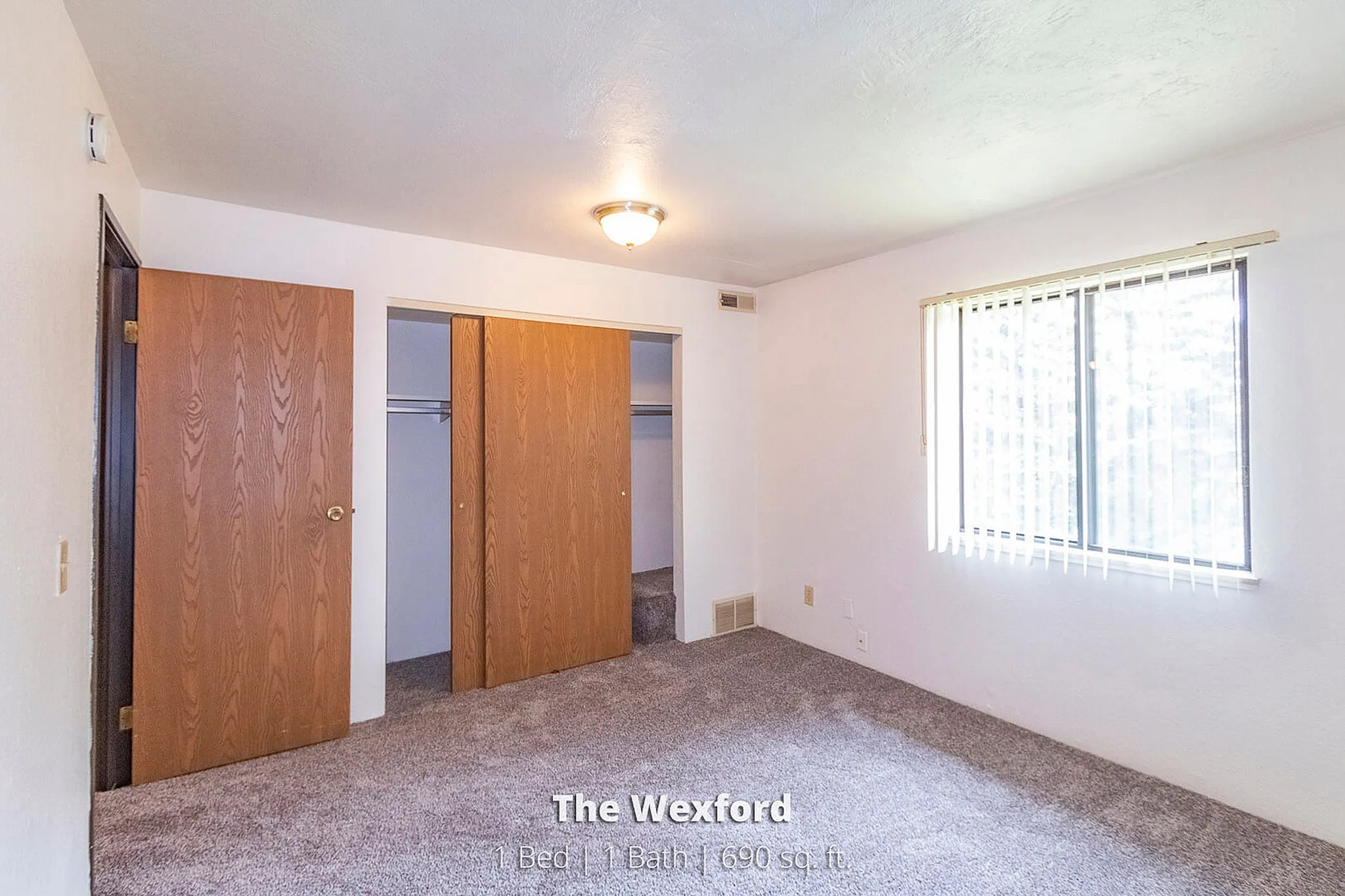 Bright and airy bedroom featuring a spacious closet and large window with vertical blinds, perfect for cozy living in The Wexford.