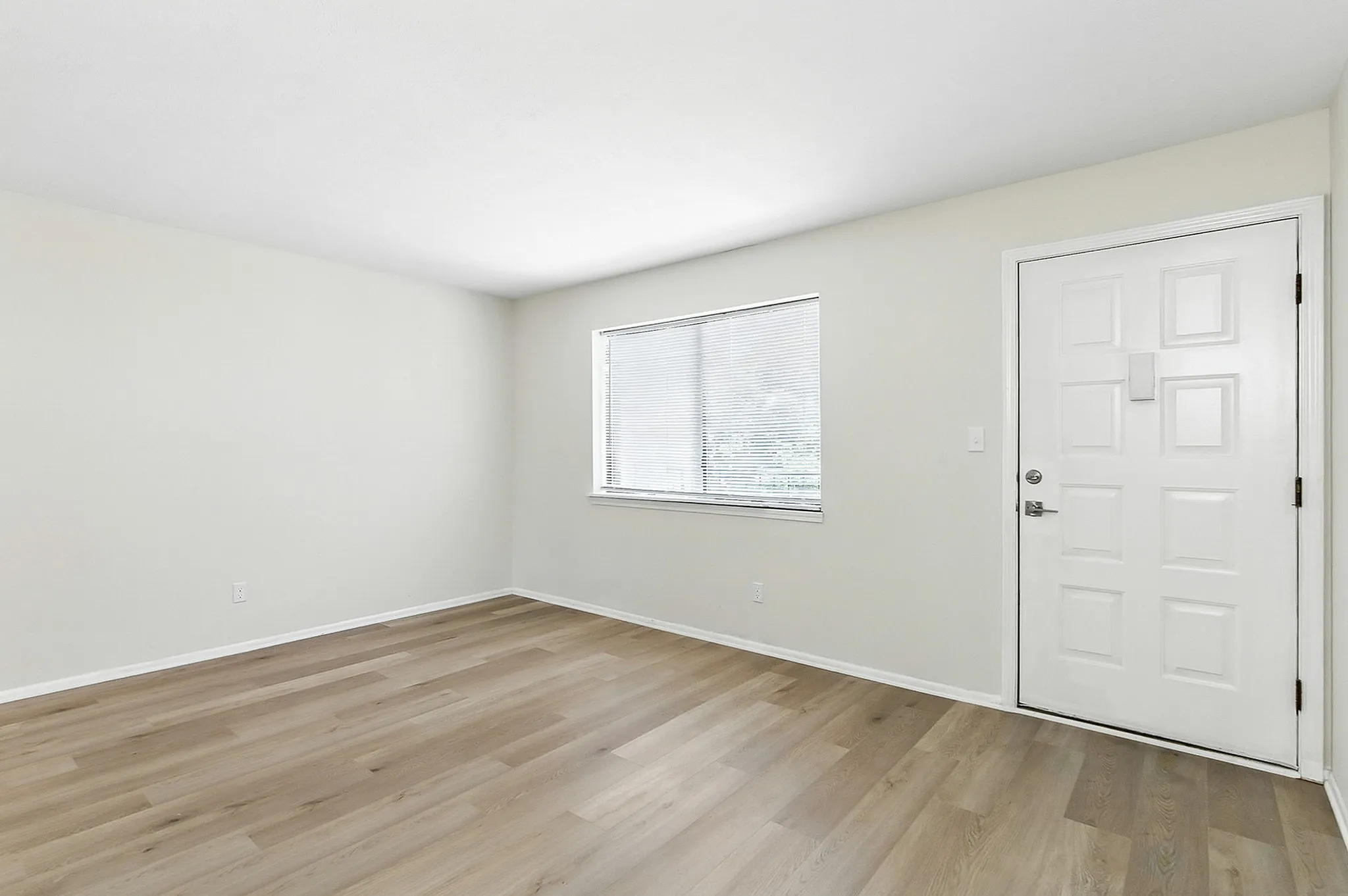 Bright and airy apartment interior featuring sleek hardwood floors, a large window for natural light, and a stylish white entry door.