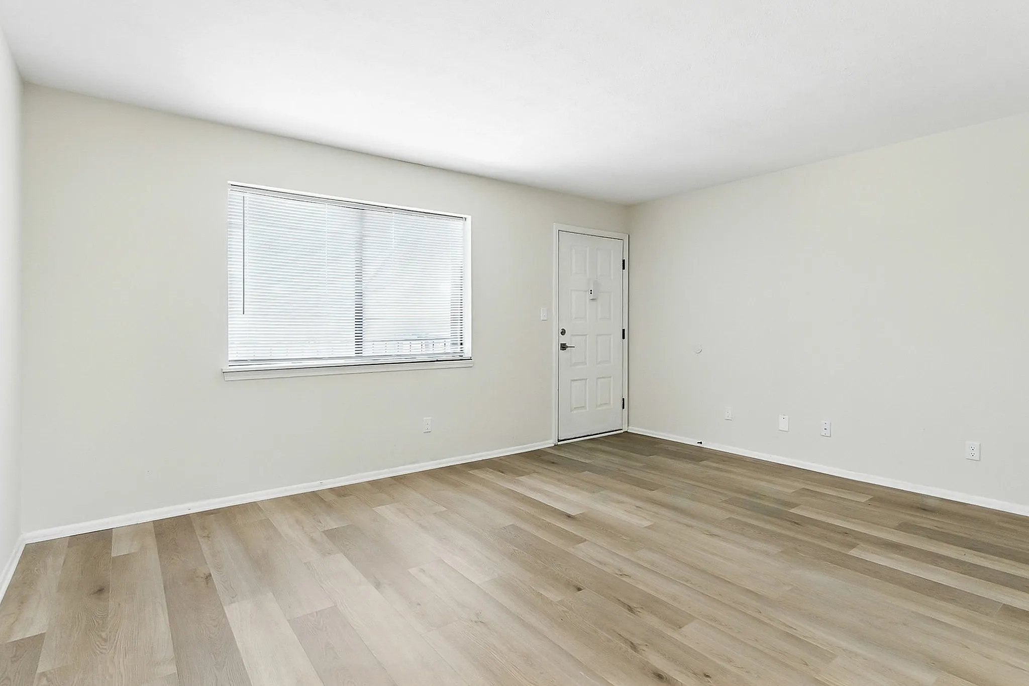 Bright and spacious living area with elegant wood flooring and large window, perfect for modern comfort.