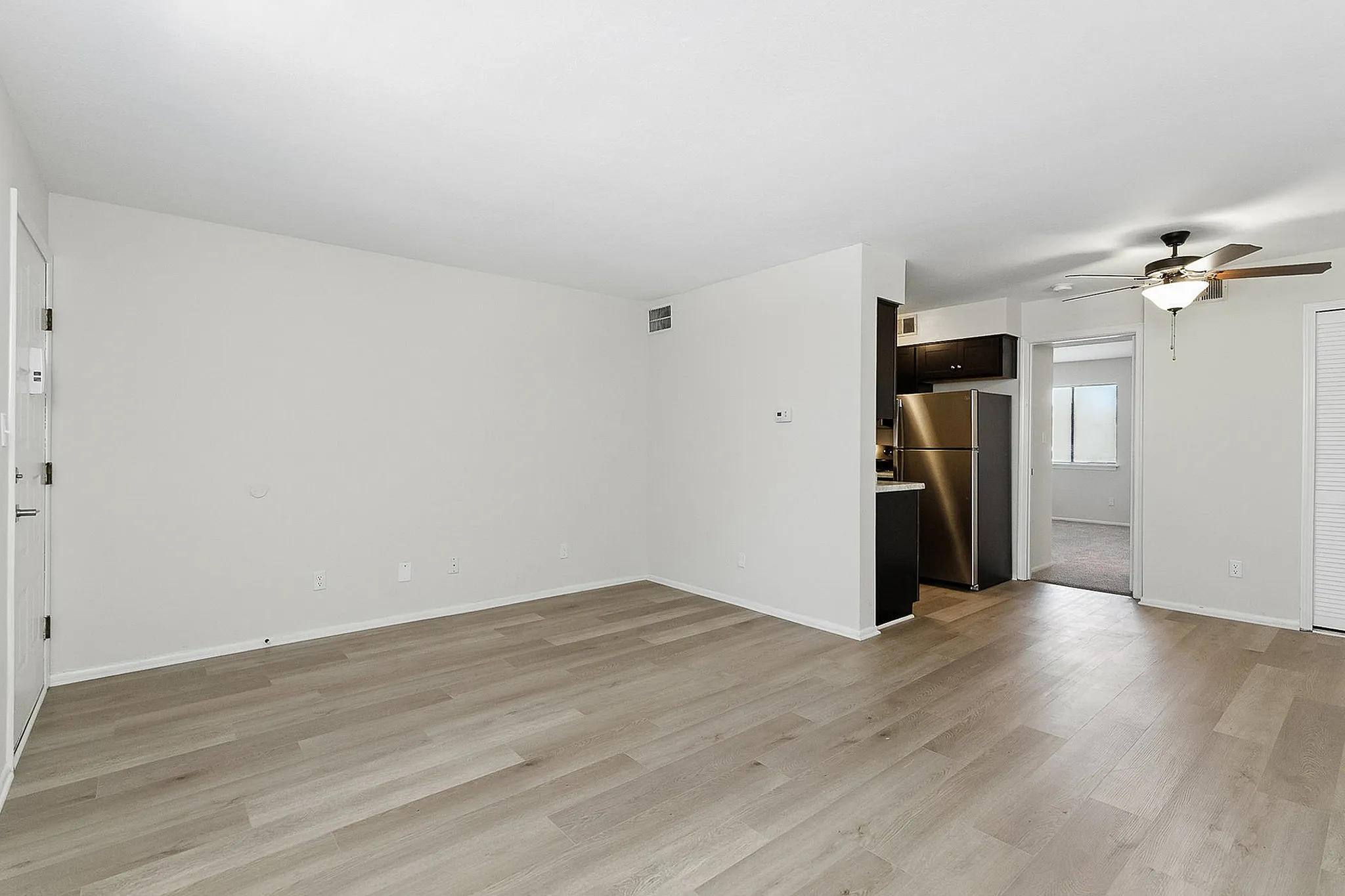 Bright and spacious living area with modern wooden flooring, connected to a stylish kitchen featuring stainless steel appliances, and ceiling fan for comfort.