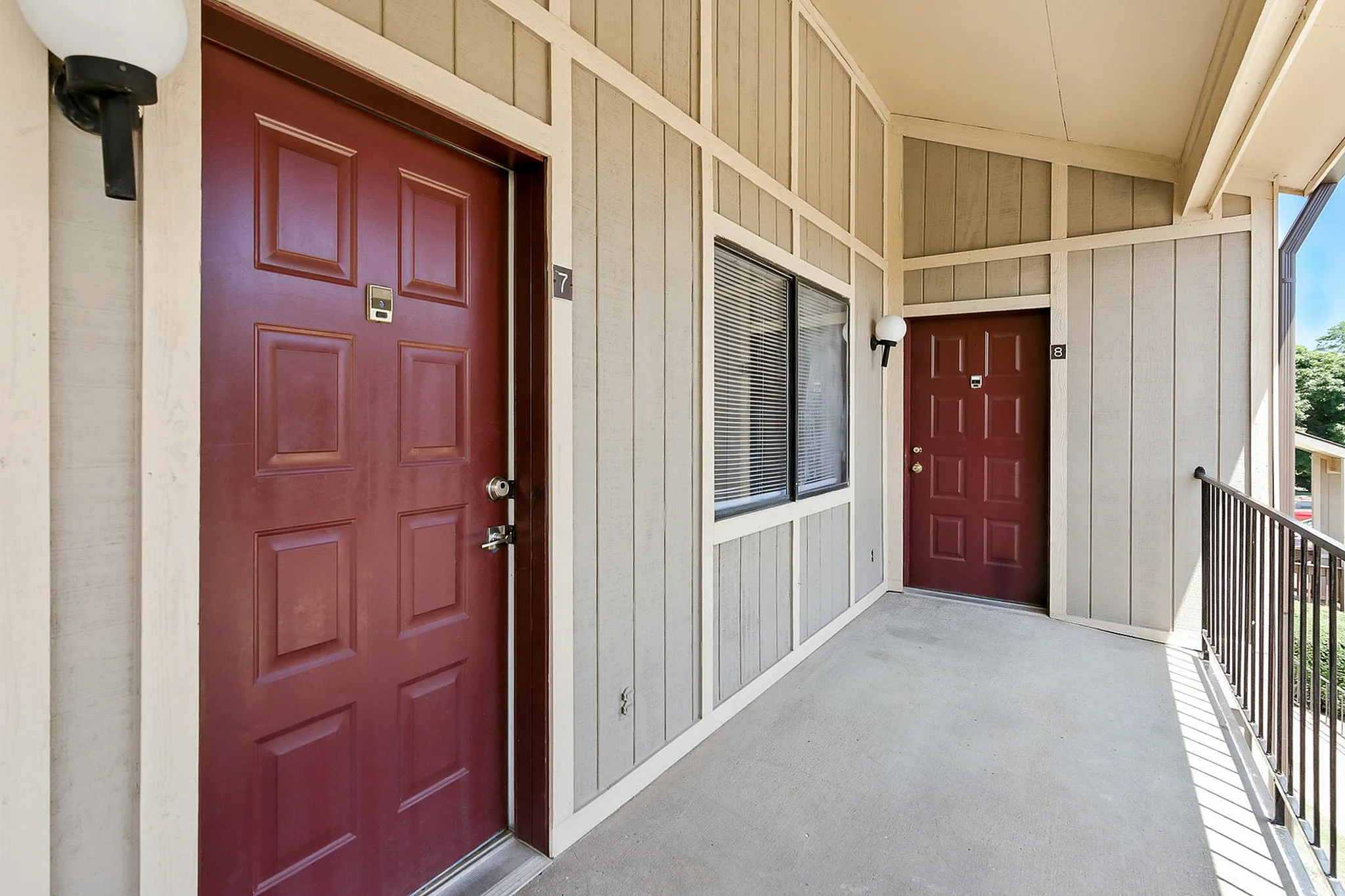 Inviting apartment entrance featuring charming wooden siding and elegant red doors, enhanced by soft exterior lighting.