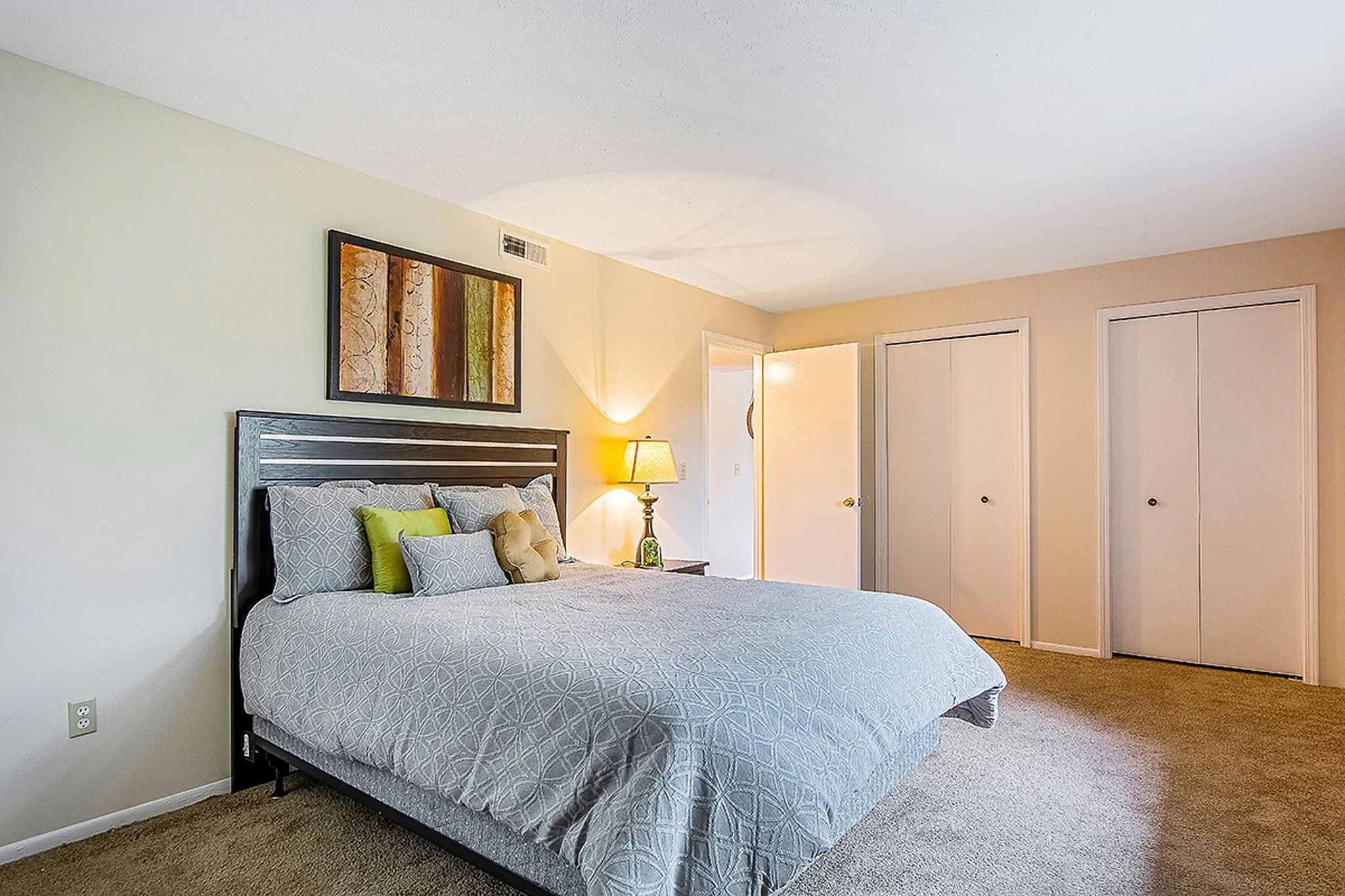 Bright and inviting bedroom with elegant bedding, decorative art, and ample closet space. Features a cozy atmosphere and stylish design.