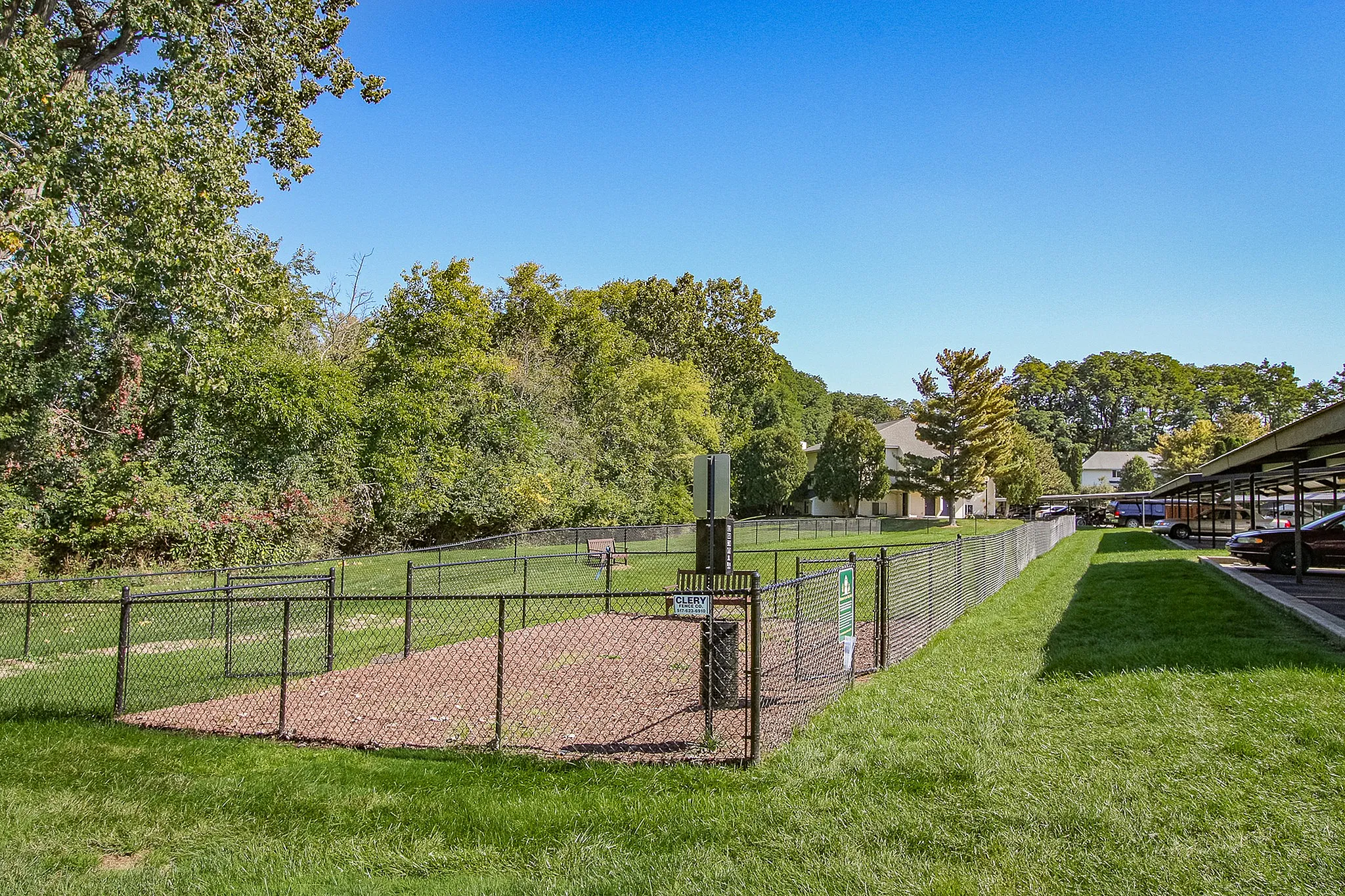 Inviting green space with fenced pet area, surrounded by lush trees and well-maintained lawns, ideal for relaxation and recreation.